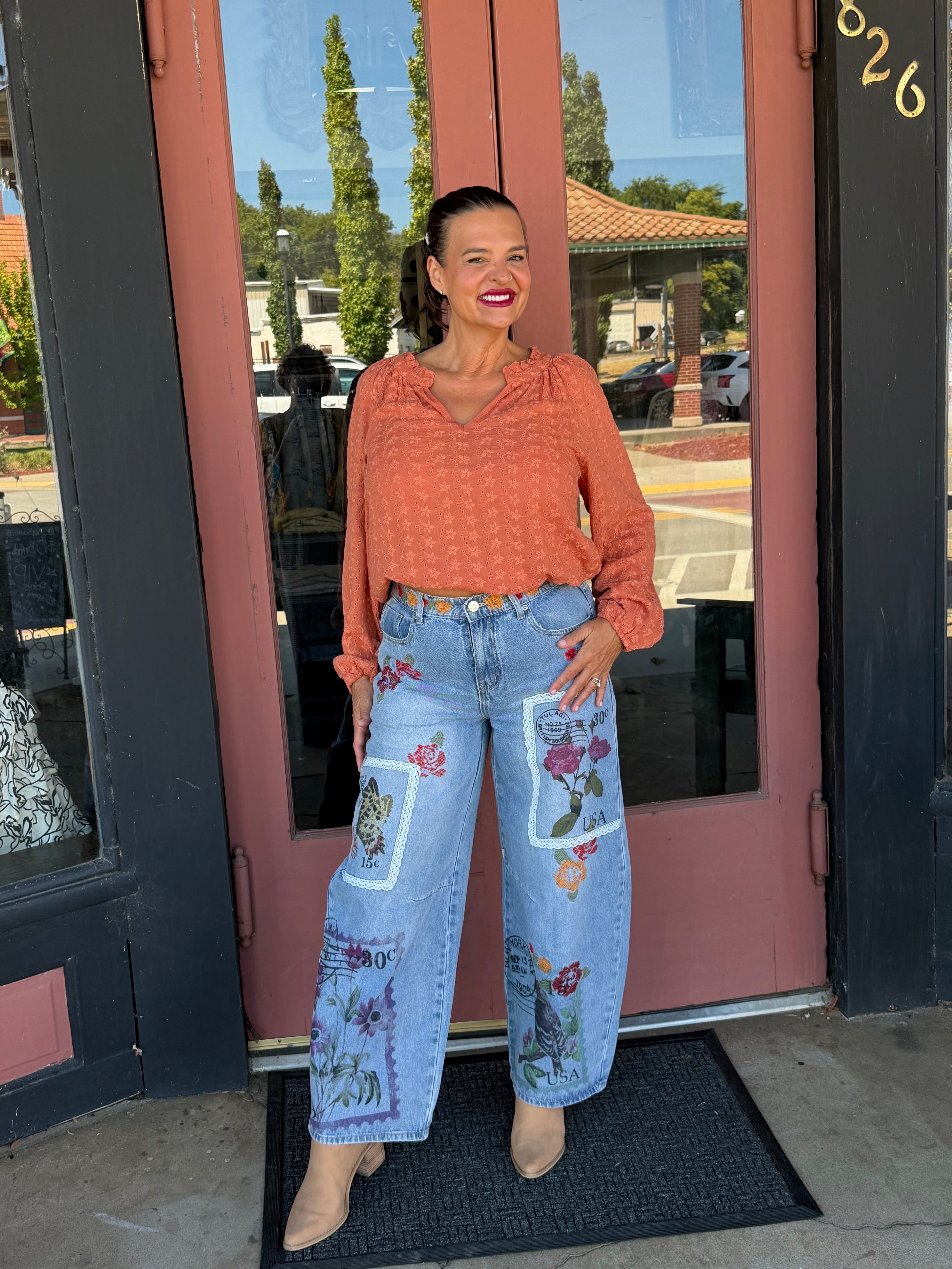 Woman in a terracotta floral eyelet blouse with ruffle neckline, side profile view showing relaxed fit and elastic cuffs, outdoors