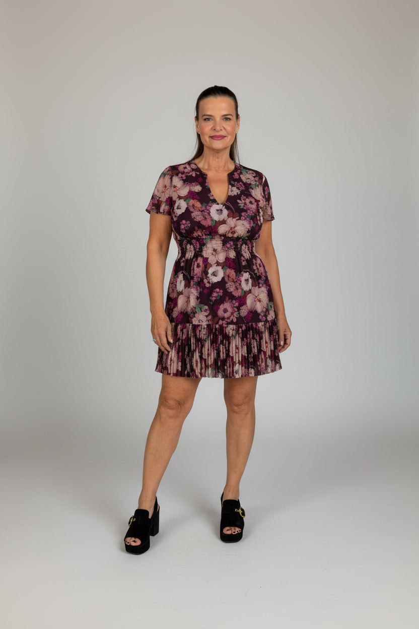 A woman wearing a short-sleeve floral mini dress with a ruffled hem and black slide sandals.