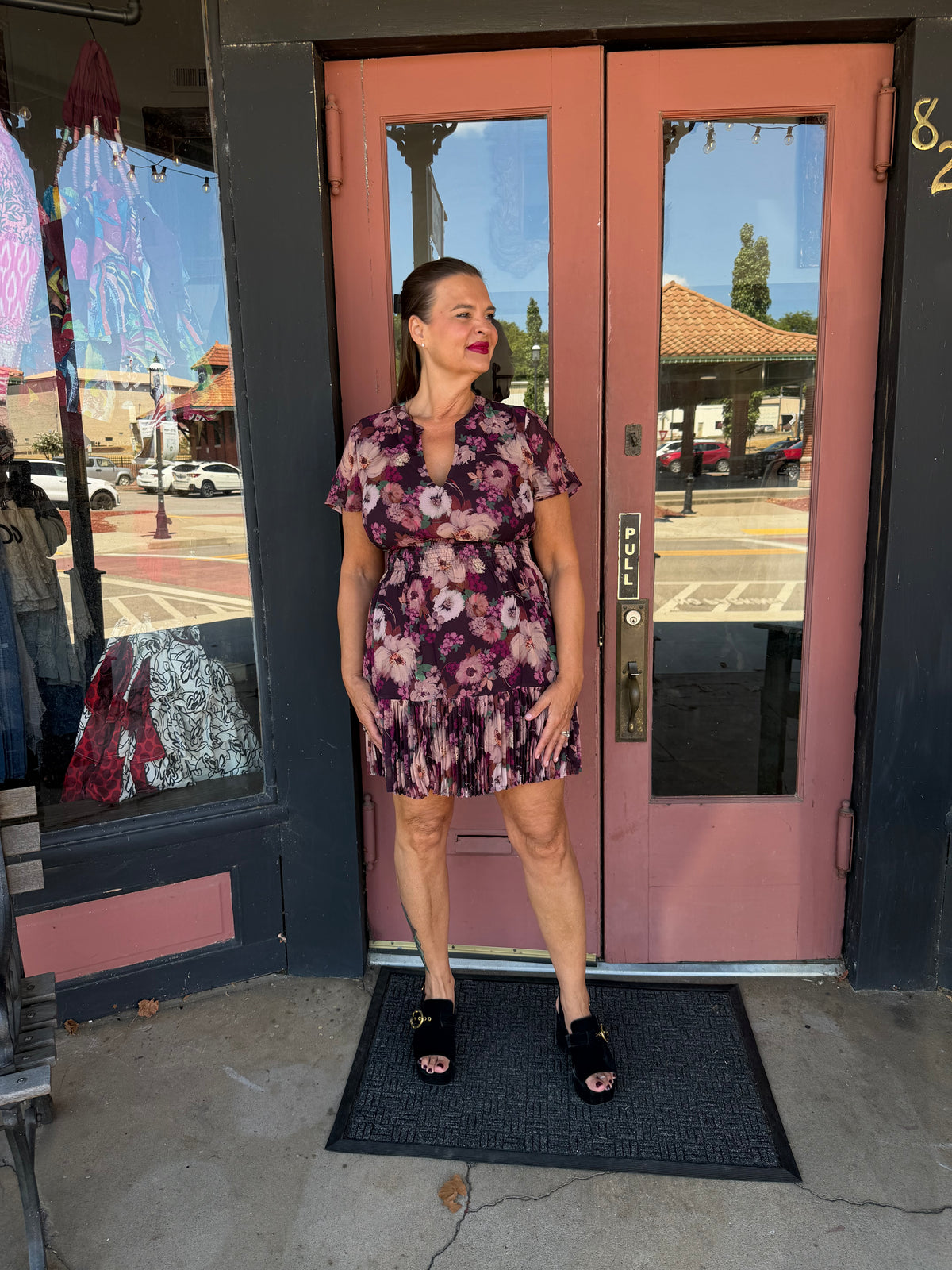 A woman wearing a short-sleeve floral mini dress with a ruffled hem and black open-toe heels.