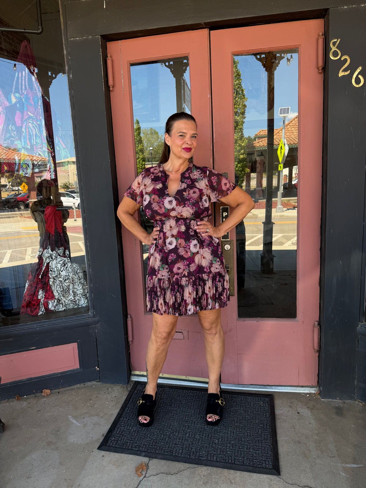 A woman wearing a short-sleeve floral mini dress with a tie waist and black platform sandals.