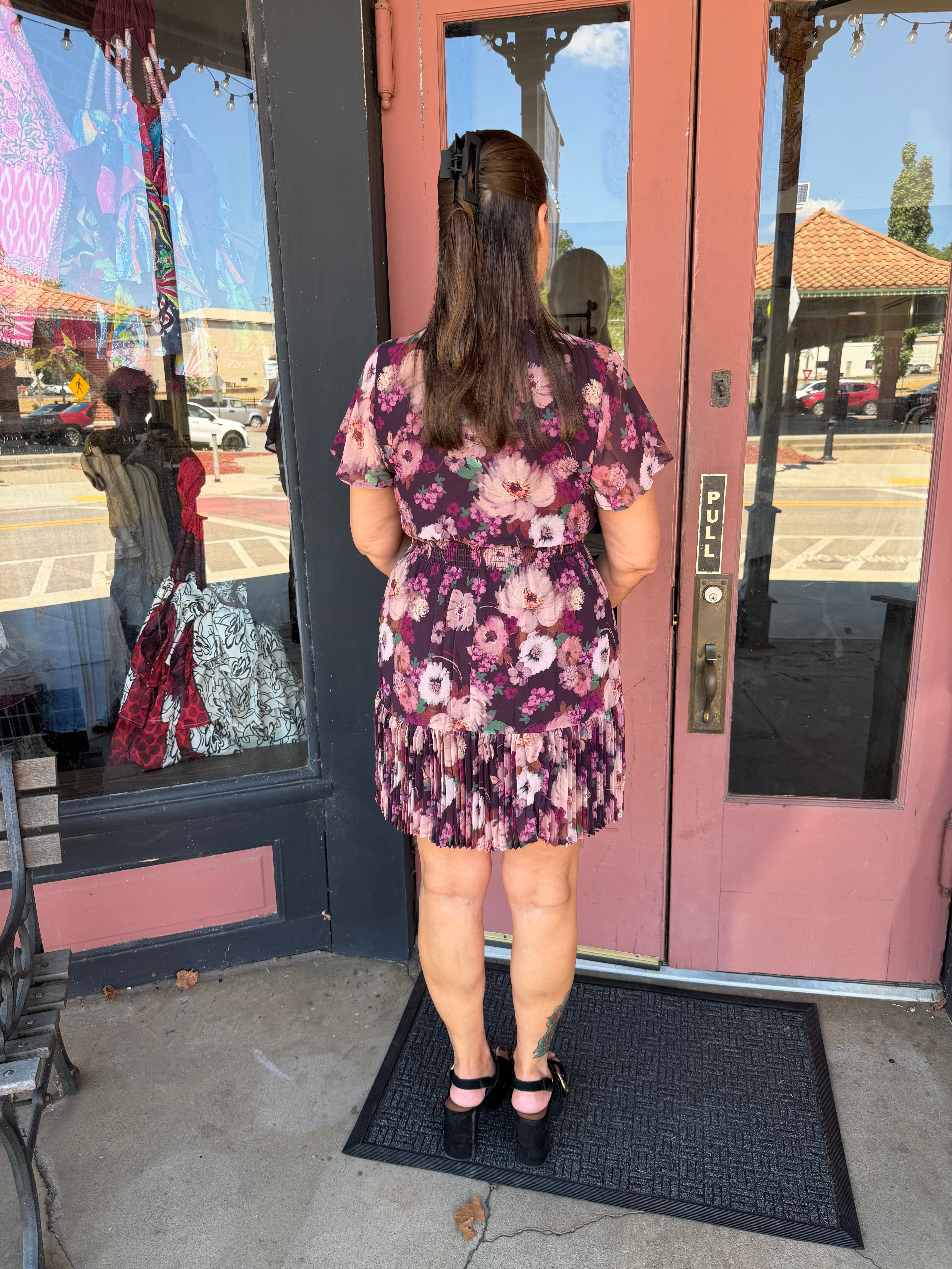 A woman viewed from behind wearing a short-sleeve floral mini dress with a ruffled hem.