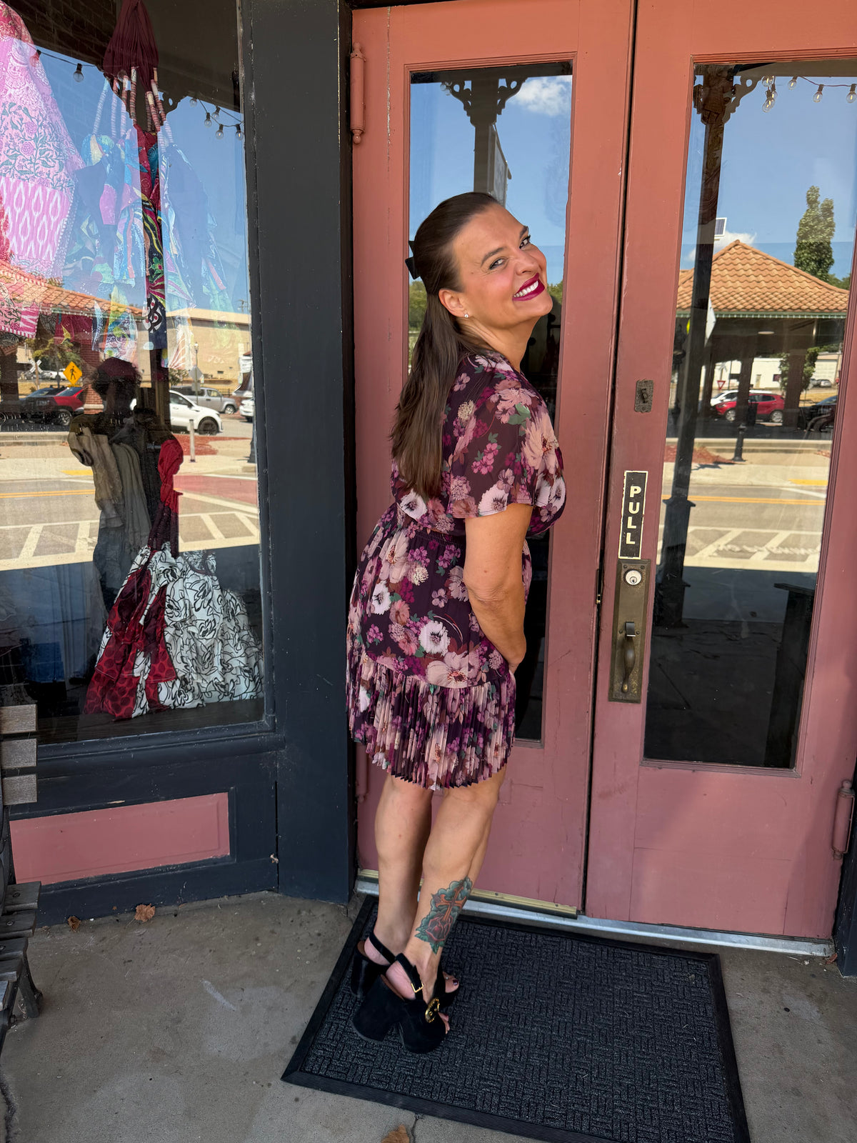 A woman wearing a short-sleeve floral mini dress with a purple, pink, and green pattern.