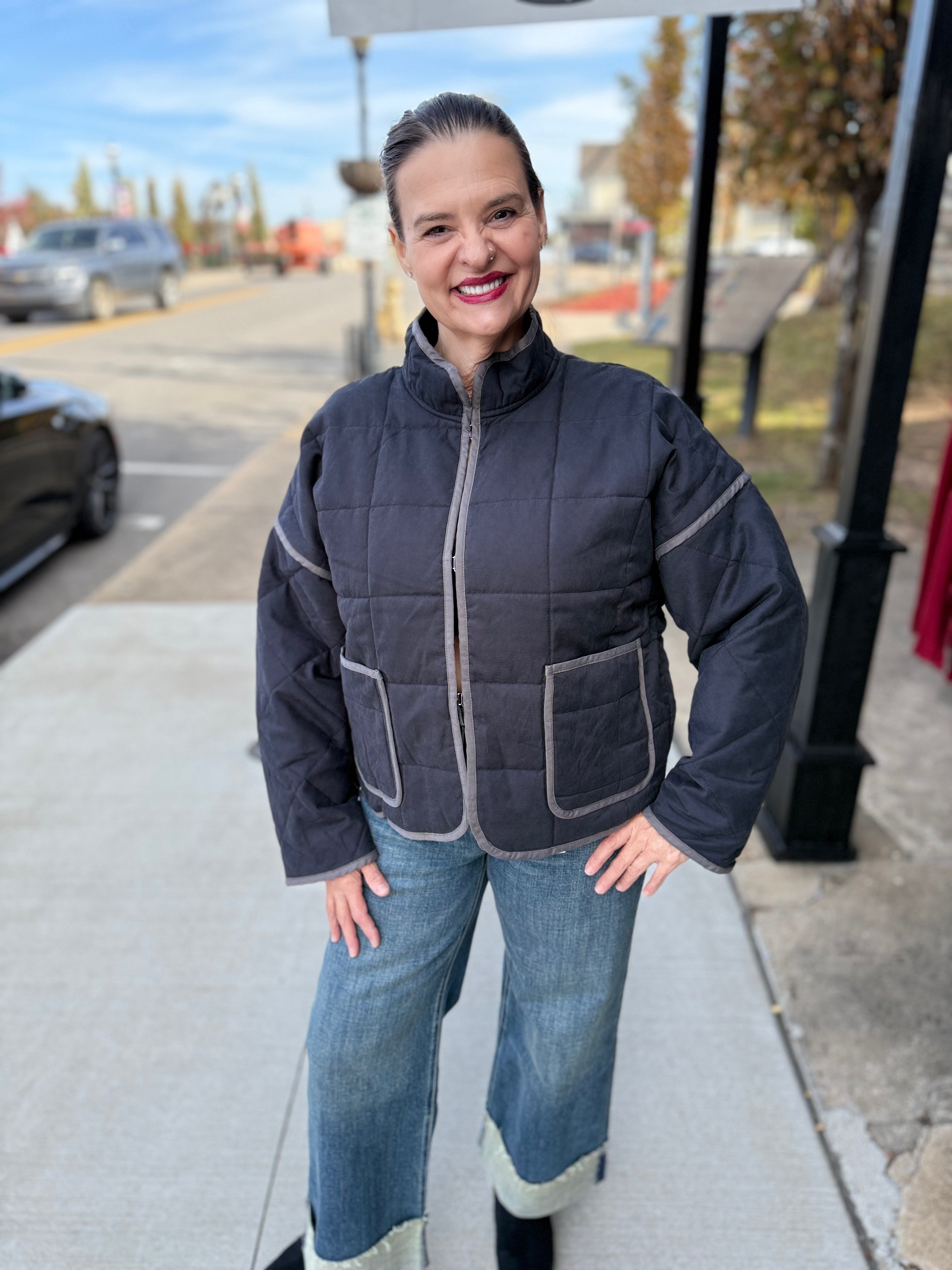 Woman wearing a dark blue quilted jacket and jeans standing on a sidewalk.