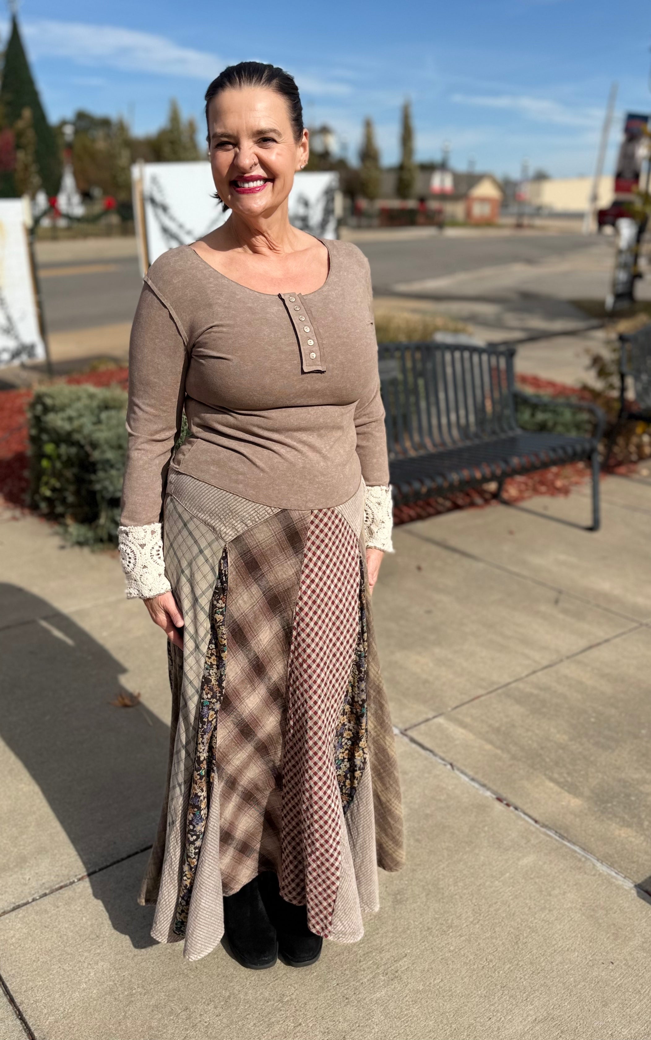 Woman in a brown dress standing on a sidewalk with a street and trees in the background
