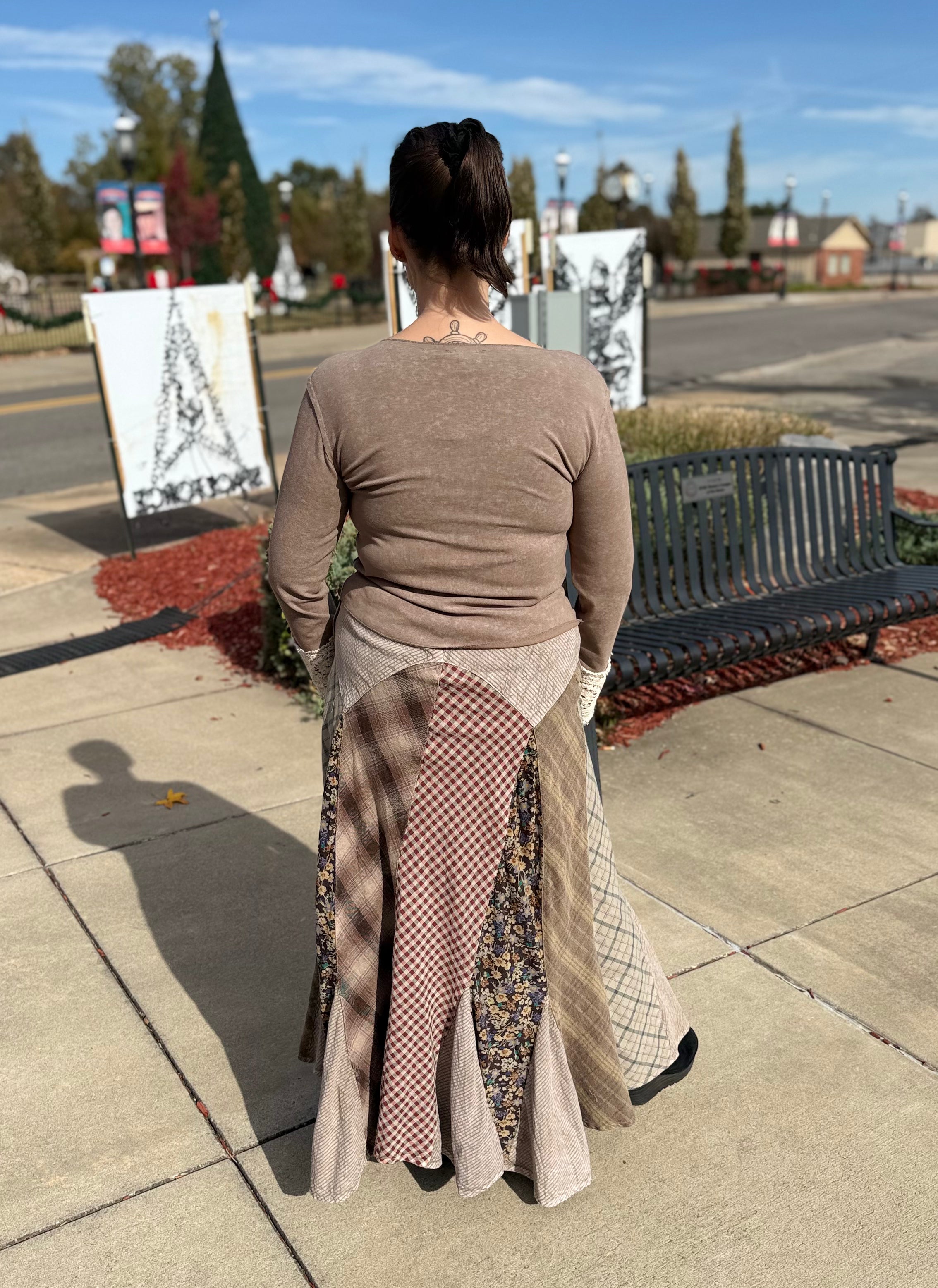 Woman walking on a sidewalk wearing a long, patterned skirt with a cityscape in the background.