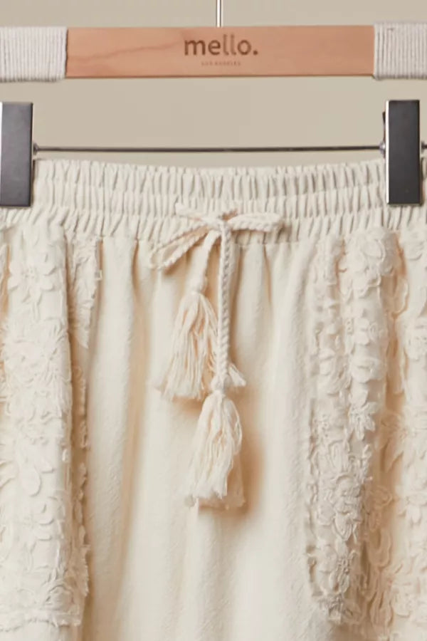 Beige pants with tassels on a hanger labeled 'mello'.