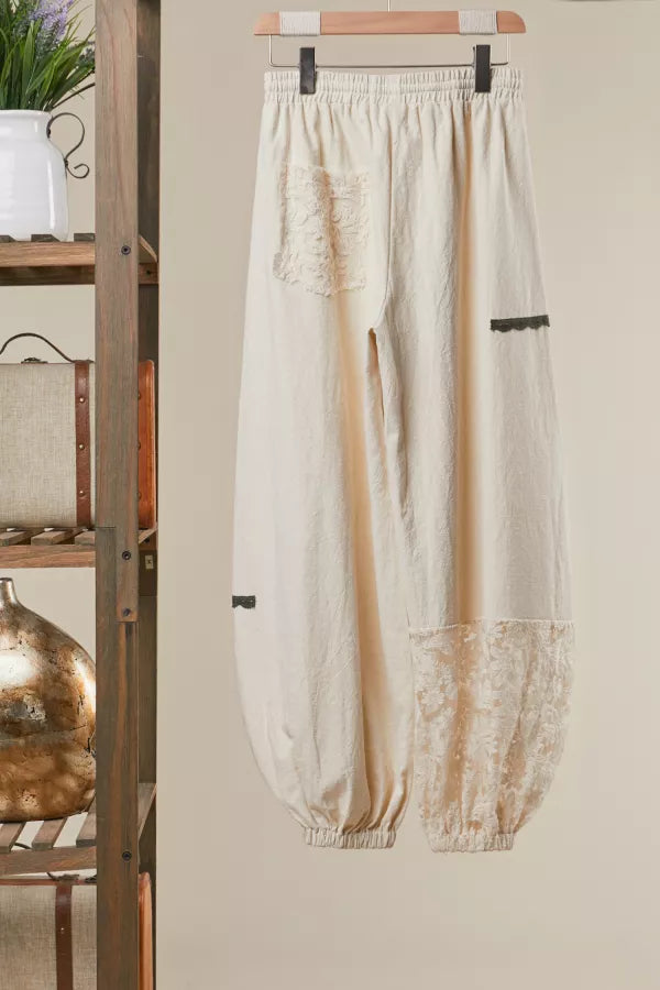 Beige pants hanging on a wooden hanger against a beige wall.