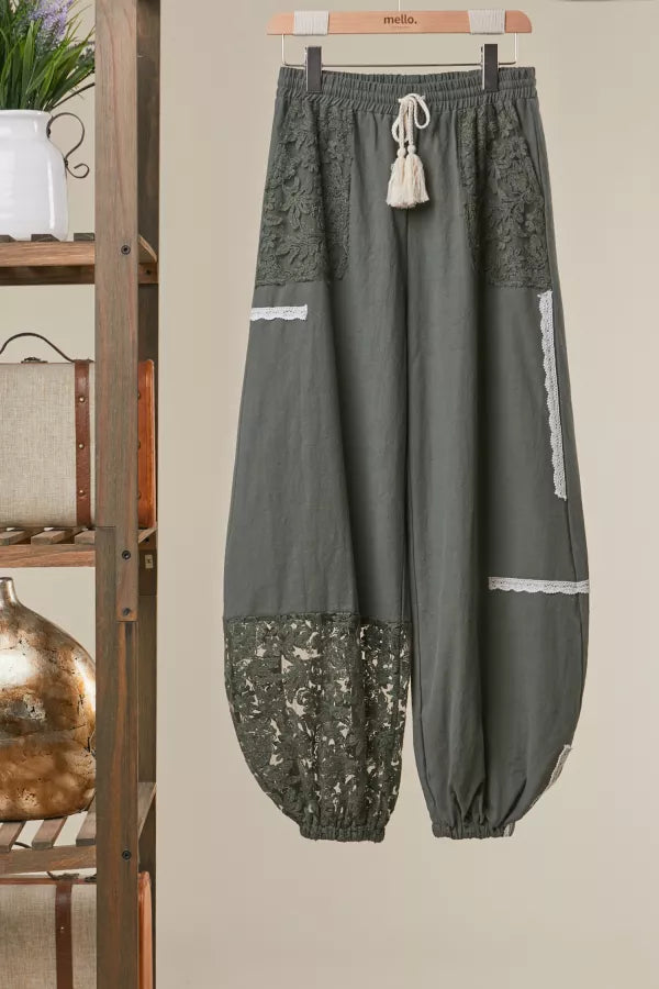 Gray pants with lace details hanging on a hanger against a beige wall.