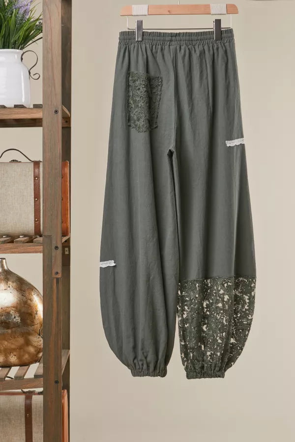 Green pants with sequin accents hanging on a wooden rack against a beige wall.