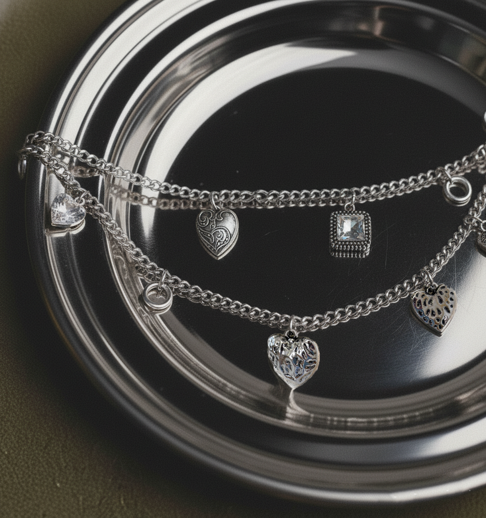 Silver bracelets with heart and square charms on a reflective surface
