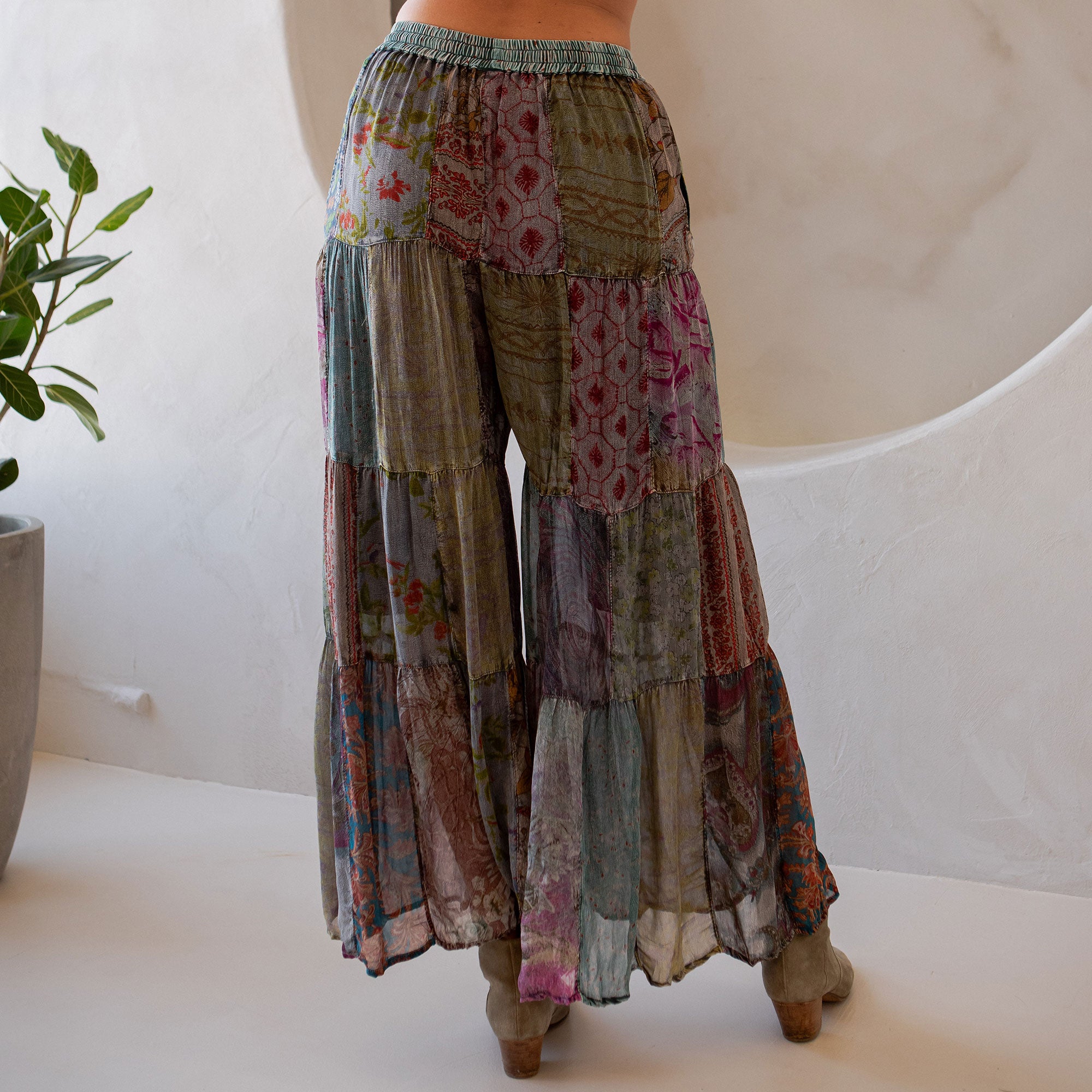 Multicolored patchwork pants with a plant and white wall in the background