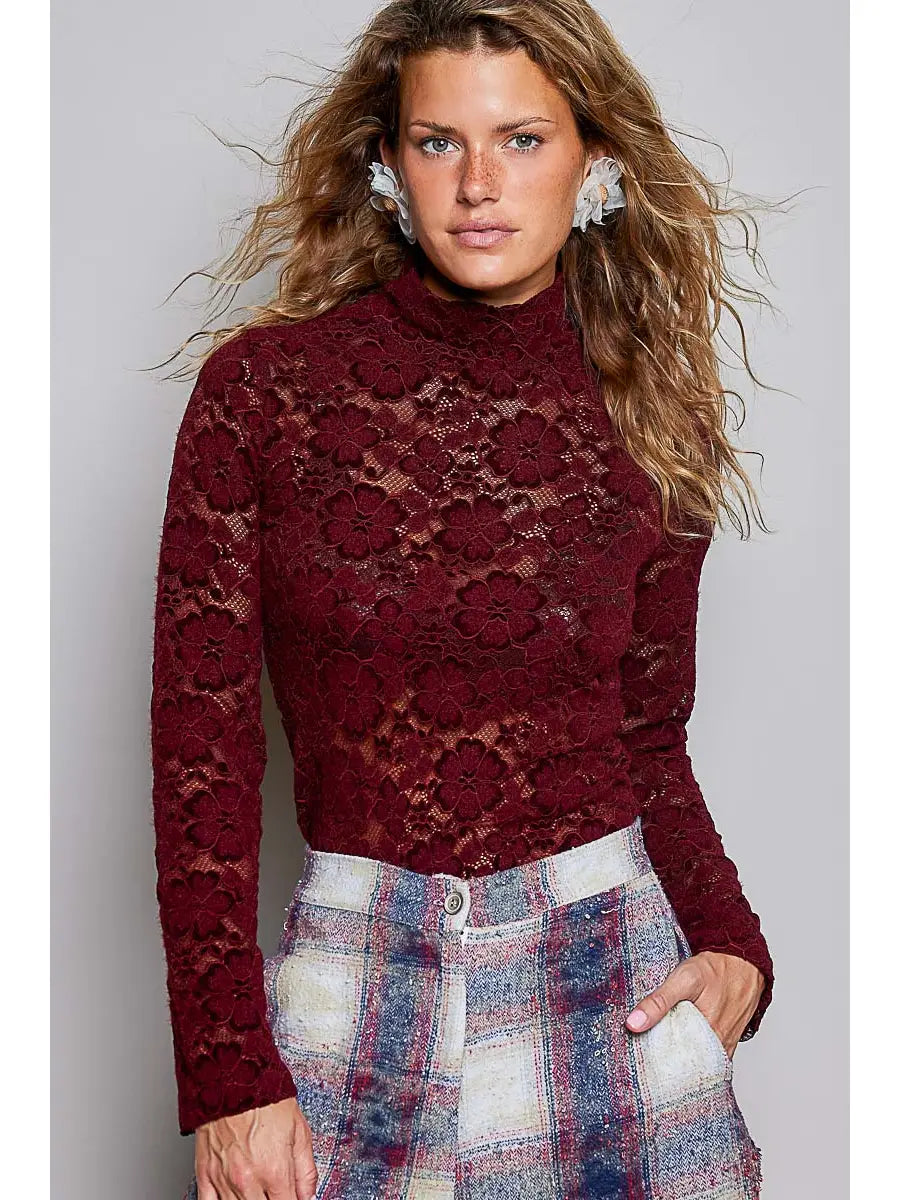 A woman modeling a long-sleeve, high-neck burgundy lace mock turtleneck top paired with a blue, red, and white plaid skirt against a solid gray studio background.