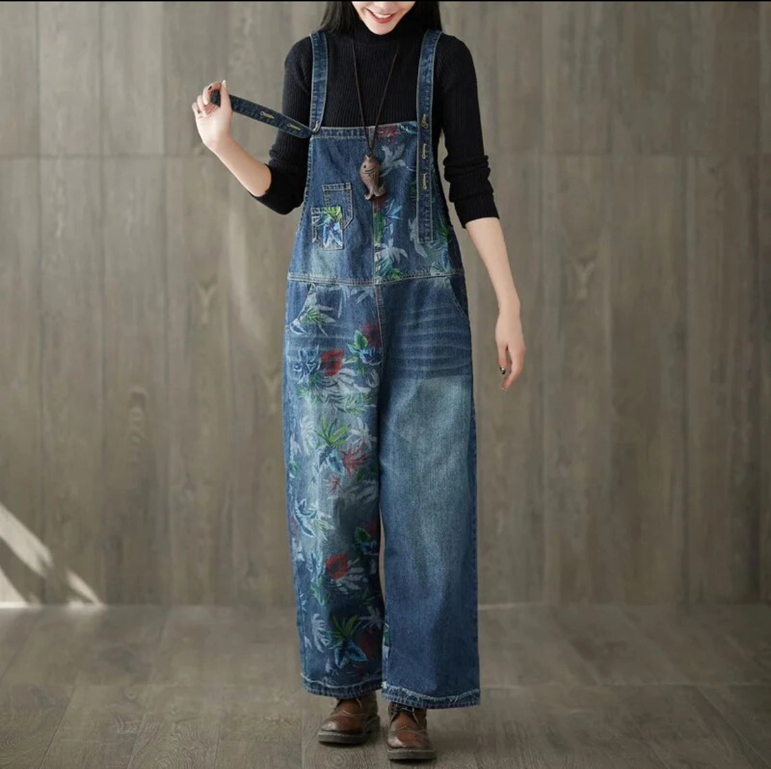 Front view wearing a floral denim  painted overalls with floral patterns against a wooden background