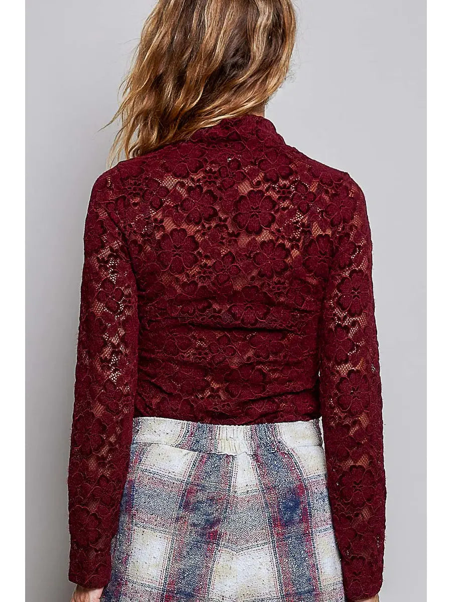 A woman viewed from the back wearing a burgundy lace long-sleeve top and a plaid skirt against a plain gray studio background.