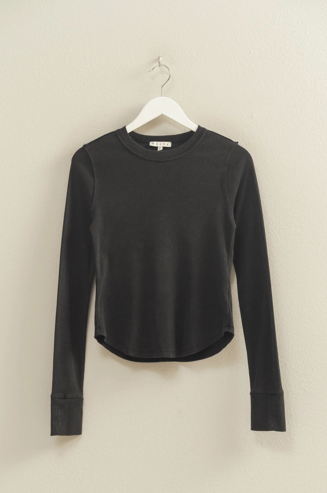 Black long-sleeve shirt on a hanger against a beige wall