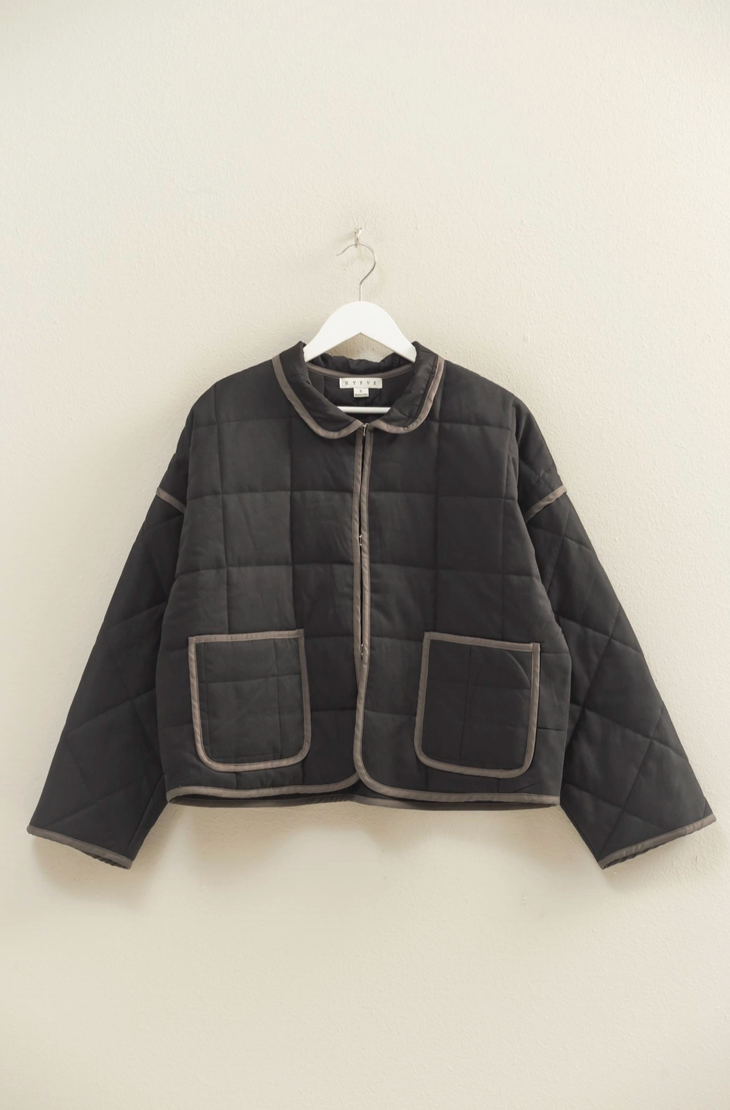Black quilted jacket on a hanger against a white wall