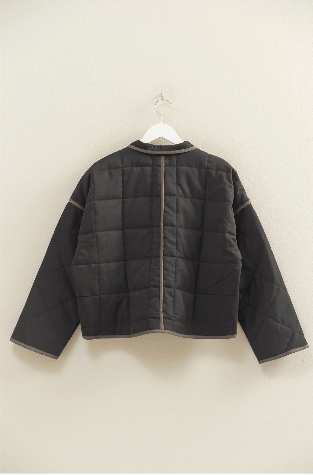 Black quilted jacket on a hanger against a white background
