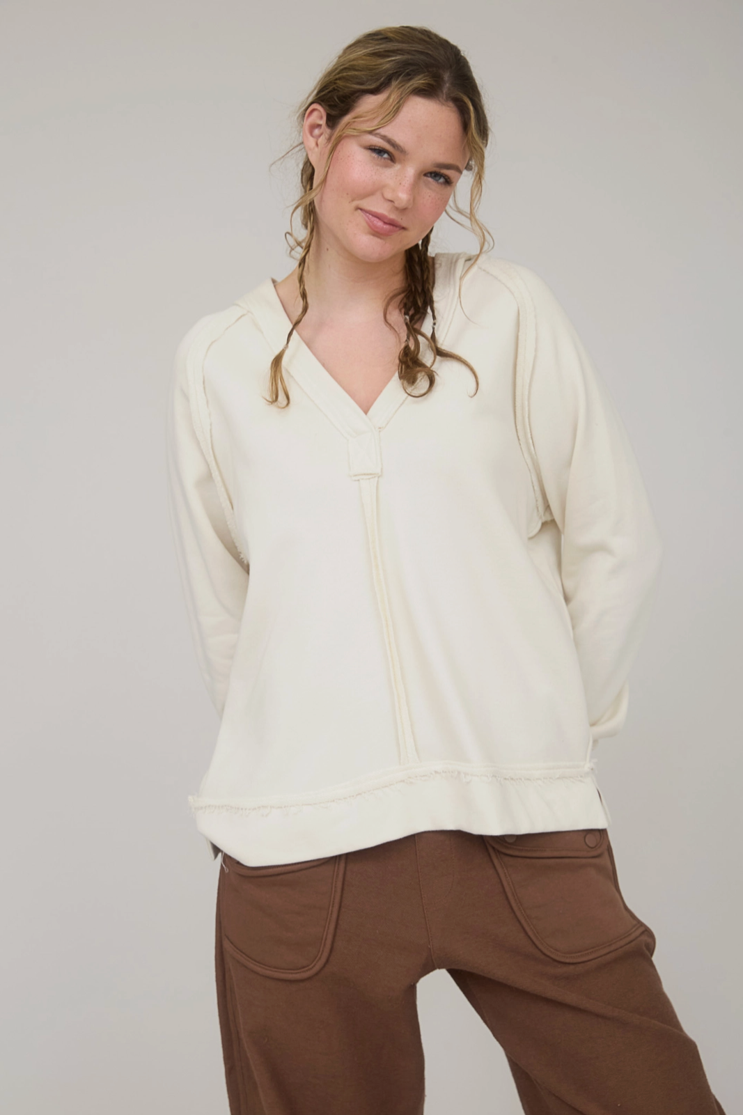 Woman wearing a cream sweater and brown pants against a plain background