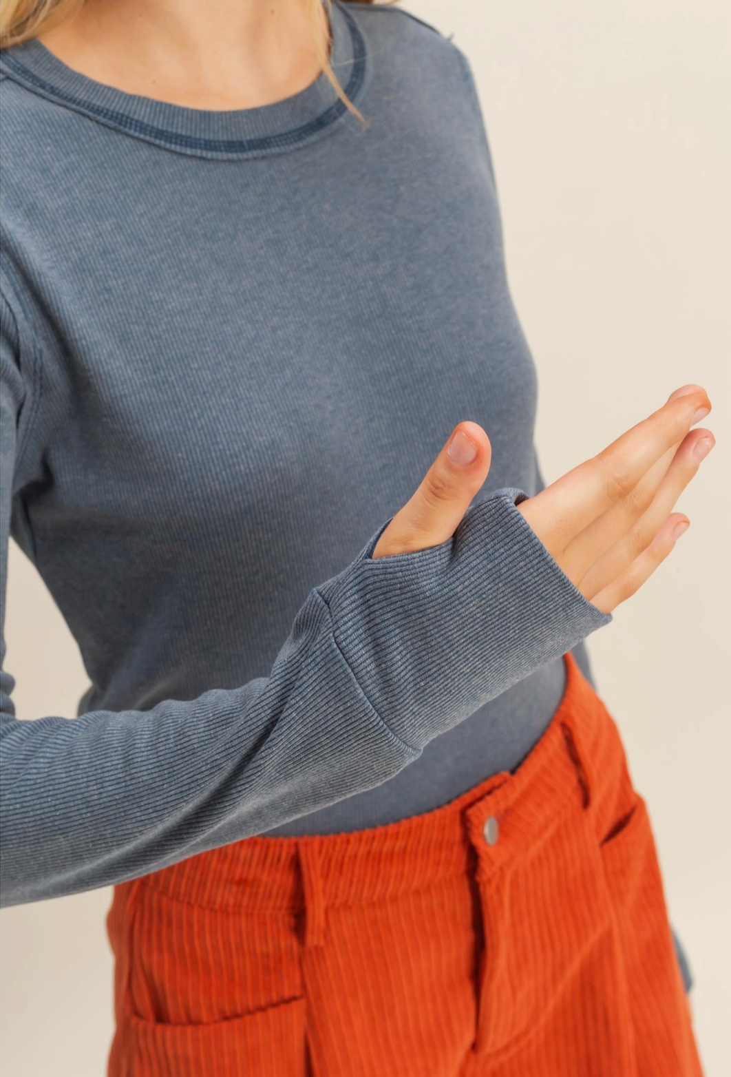 Person wearing a blue sweater and orange pants against a beige background