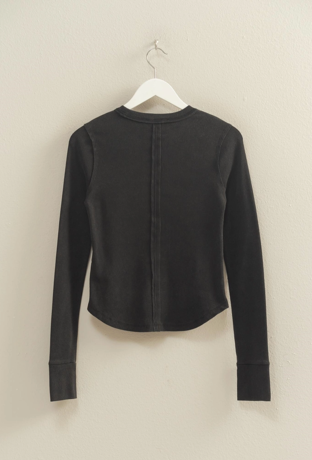 Black long-sleeve top on a hanger against a beige background