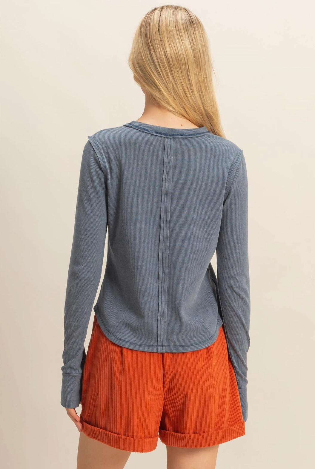 Person wearing a blue long-sleeve top and orange shorts on a beige background