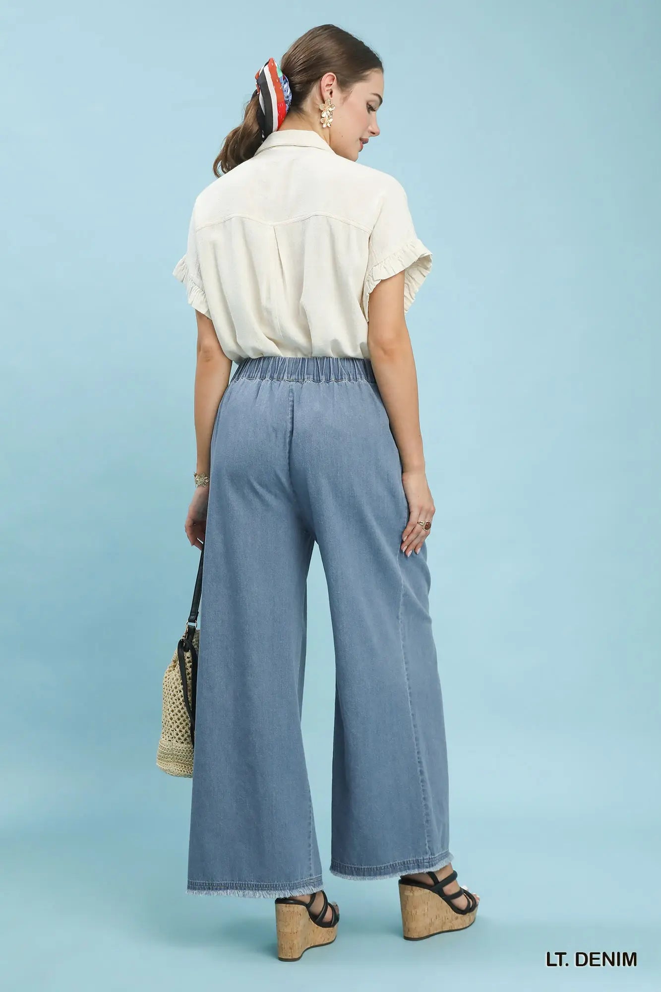 Woman wearing light denim pants and a white shirt against a blue background