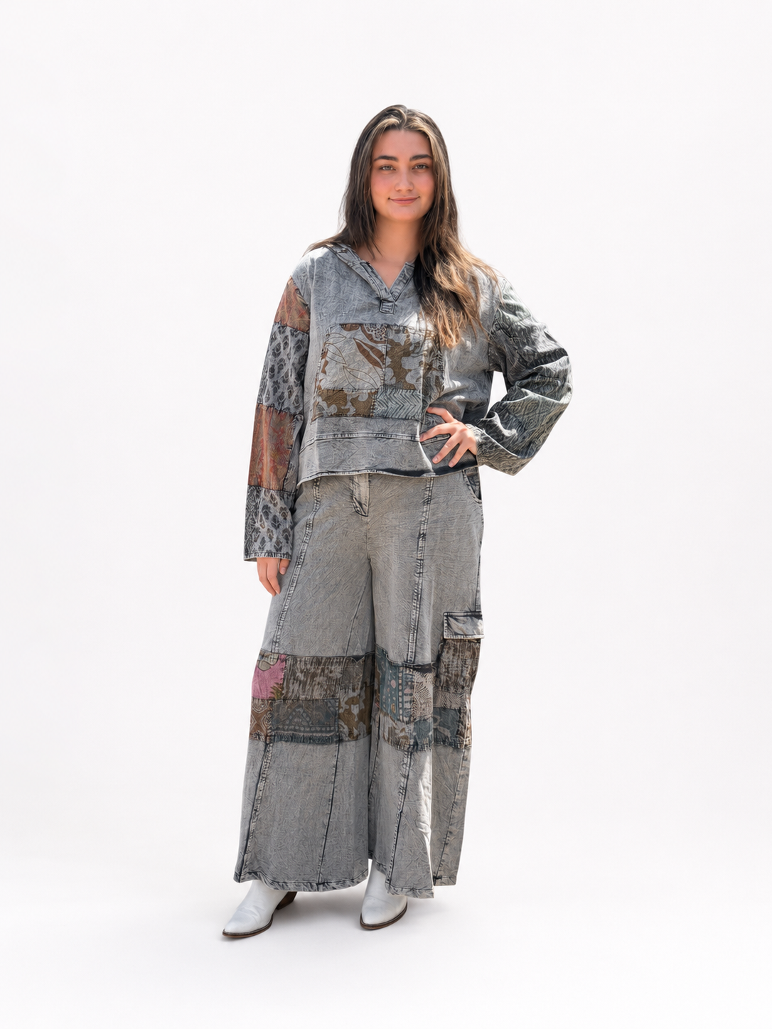 A woman modeling a matching patchwork denim set consisting of a cropped long-sleeve top and wide-leg pants, styled with white boots against a plain white studio background.