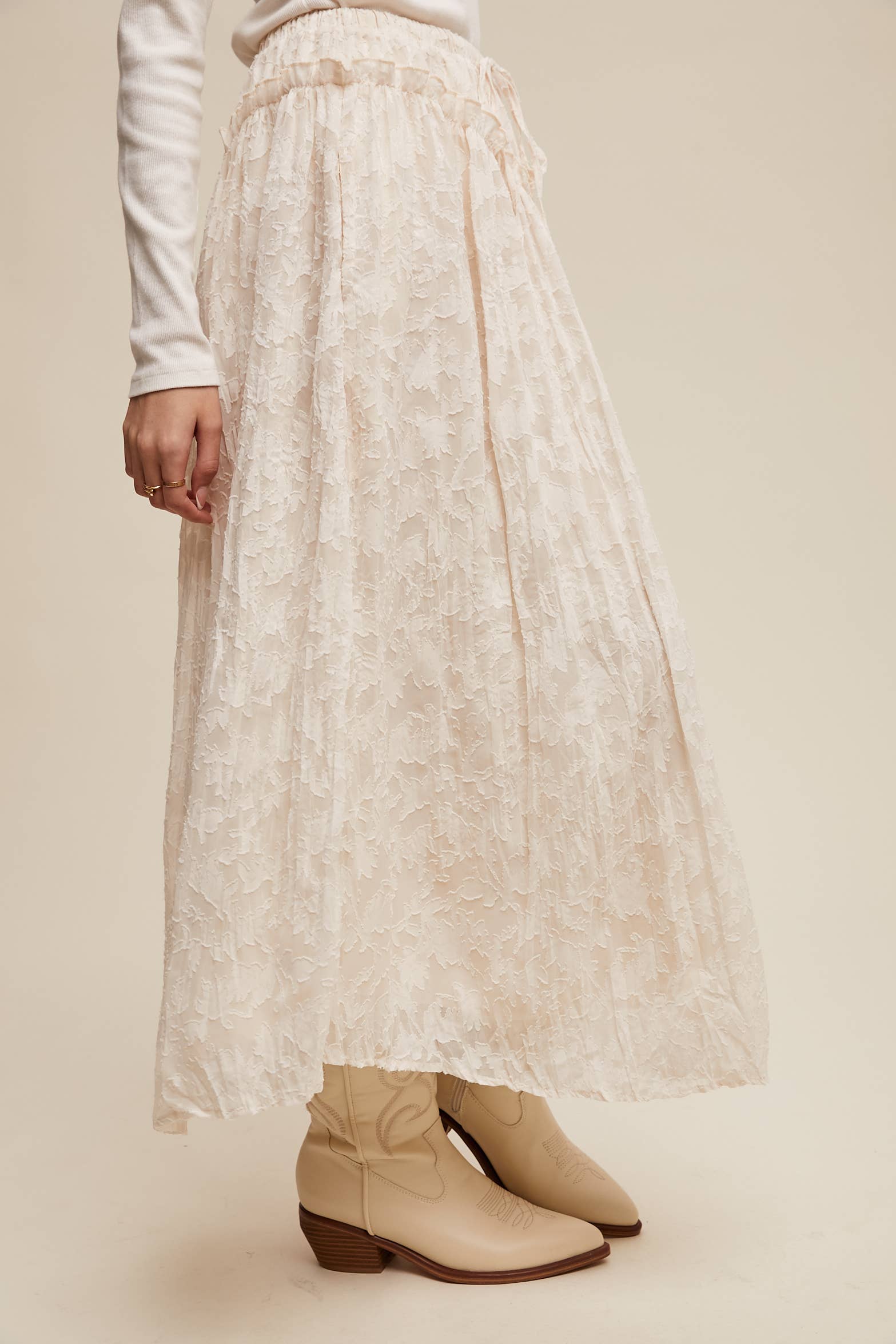 Ivory floral lace maxi skirt with elastic drawstring waist and ruffle detail, ankle-length bubble hem; shown on model with cream western boots.