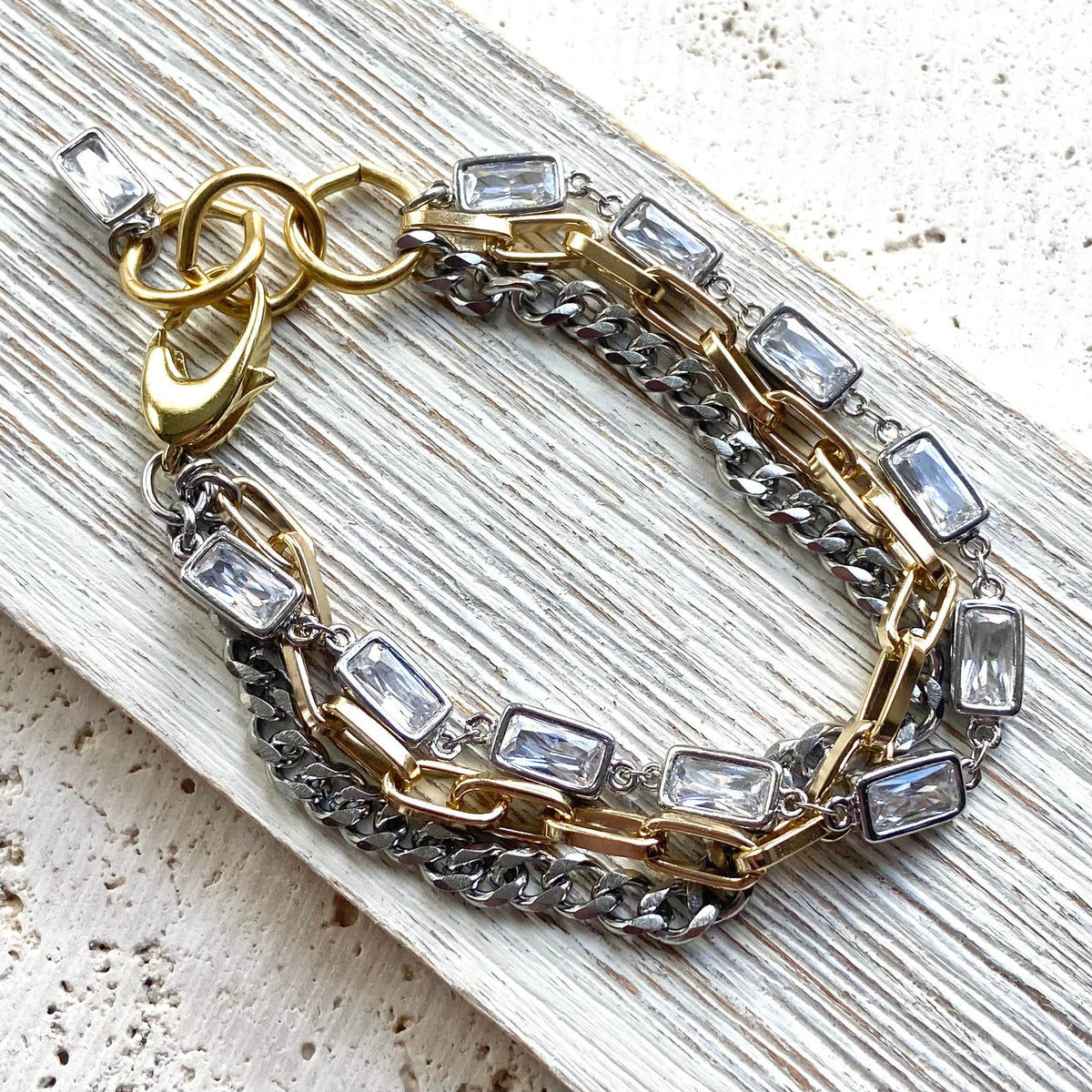 Bracelet with gold and silver chain links and clear gemstones on a textured surface