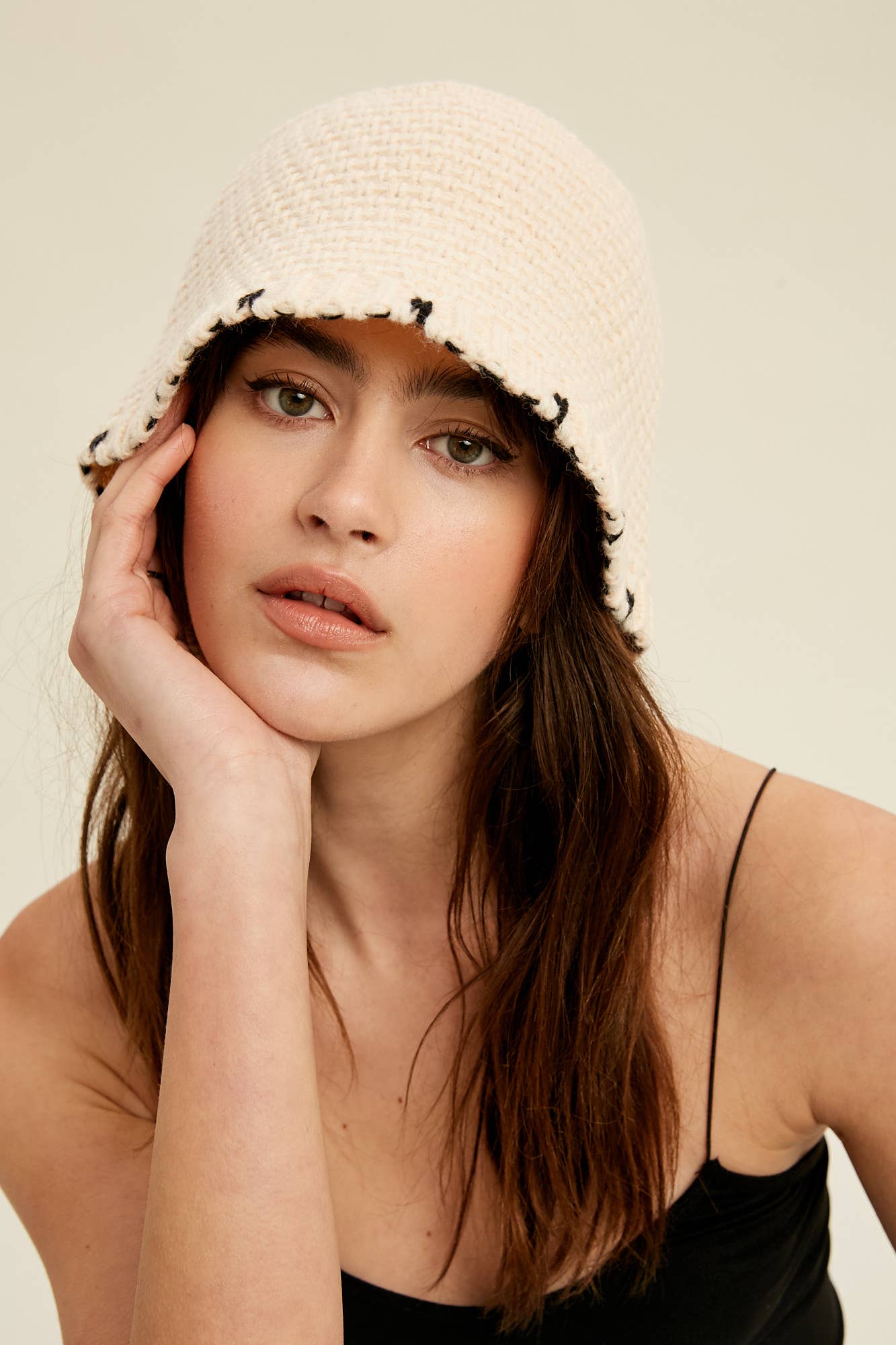 Close-up — cream knit bucket hat with contrast black whipstitch edging and soft brim, on model.