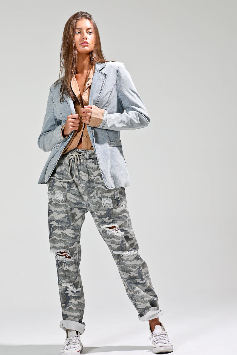 Front view of model styling light-wash denim blazer with tan shirt and distressed camo joggers for a boho-street look.
