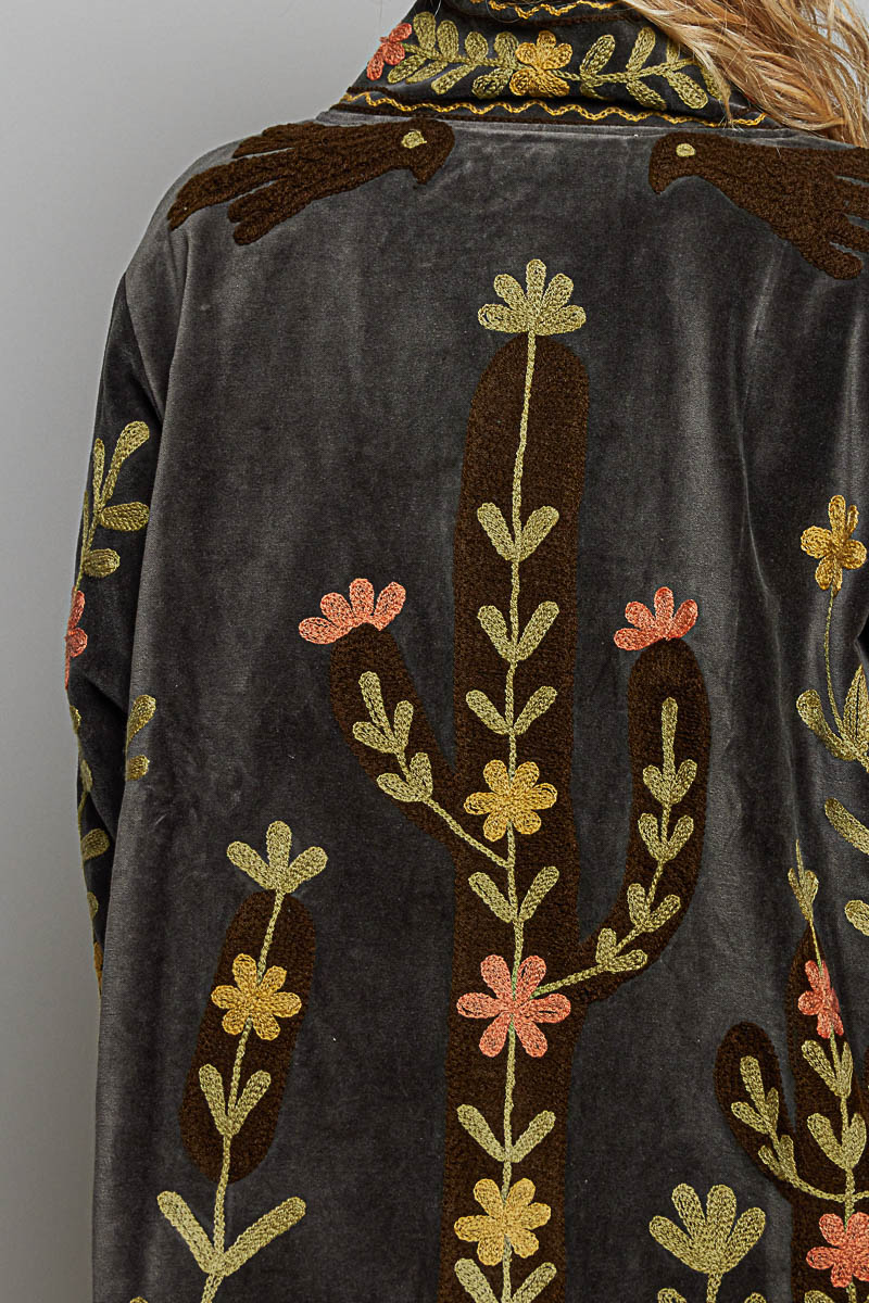 Close-up of a dark gray velvet jacket featuring embroidered cactus and floral patterns in gold, brown, and coral pink.