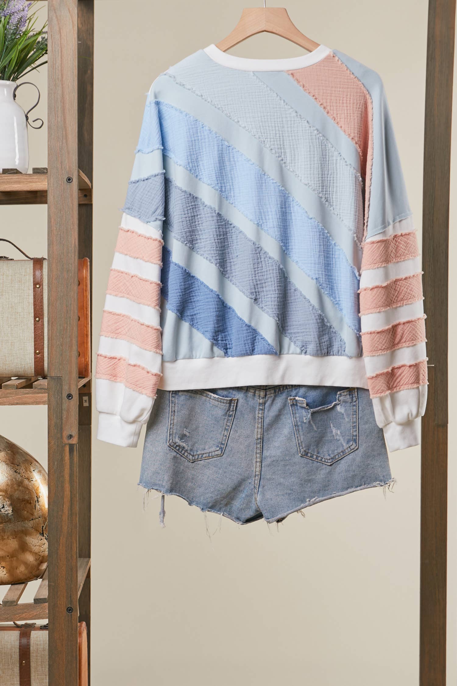 Colorful striped sweater over denim shorts on a hanger against a neutral wall.