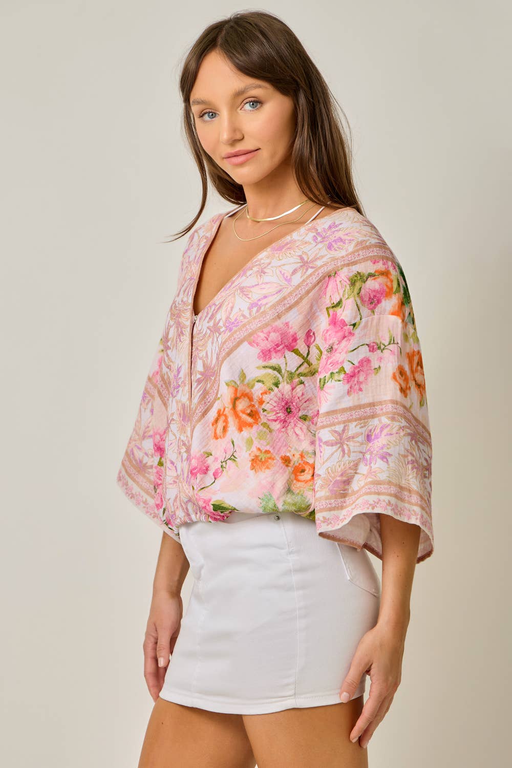 Woman wearing a floral blouse and white skirt against a plain background