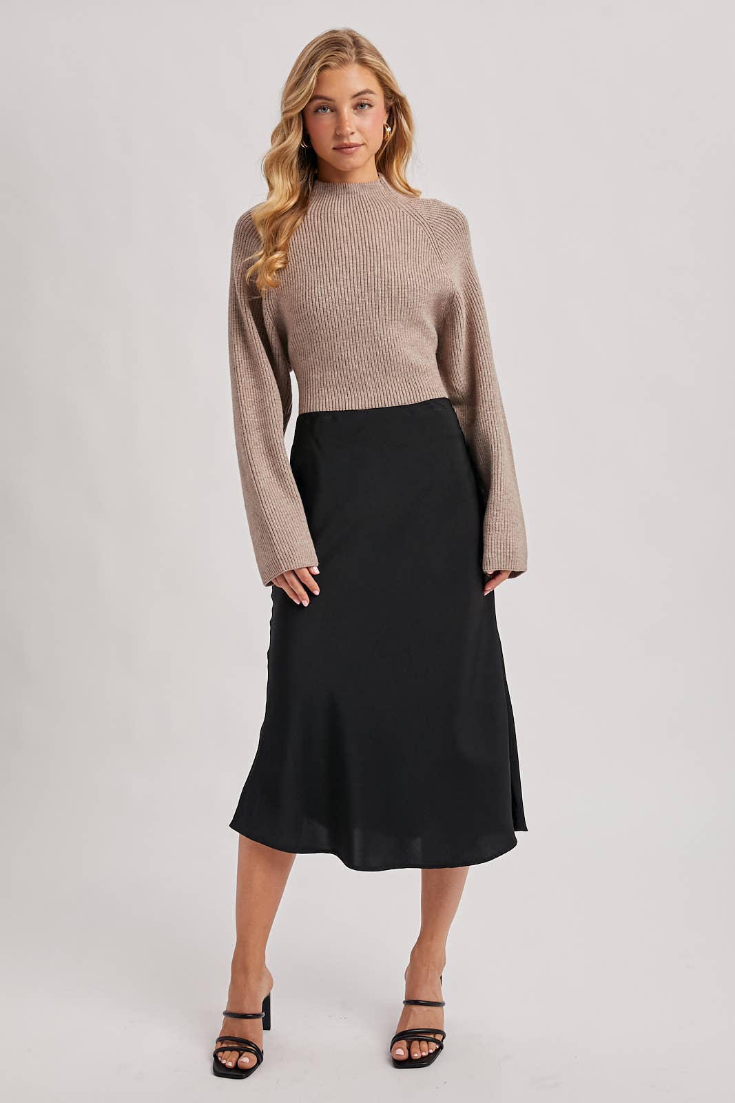 Taupe ribbed mock-neck sweater with wide long sleeves and a cropped fit, styled with a black skirt.