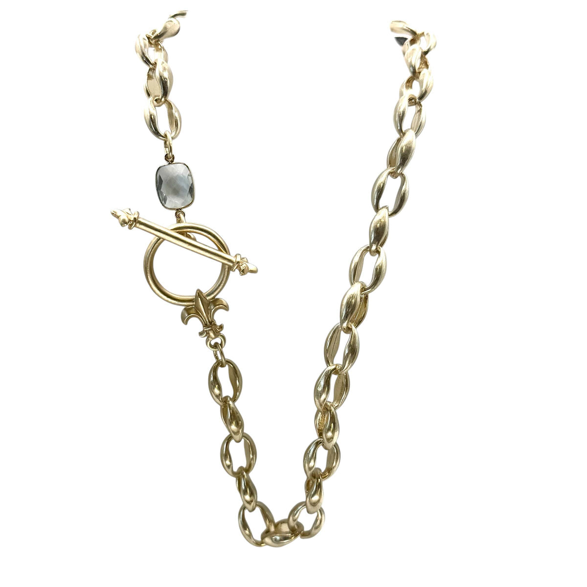A gold-toned chain necklace with a distinctive toggle clasp featuring a round ring, a decorative fleur-de-lis, and a small gray stone accent, shown on a plain white background.
