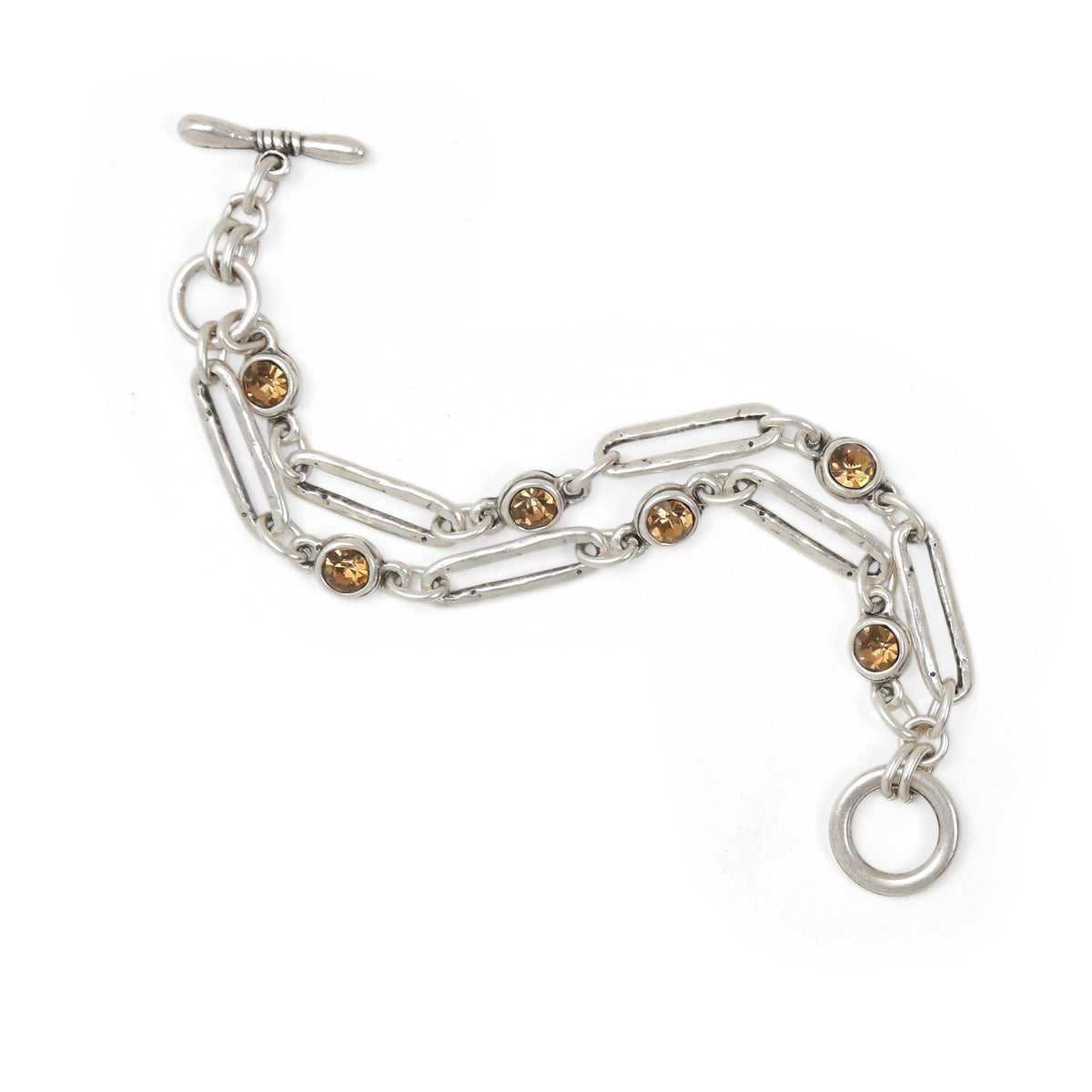 A silver-toned chain bracelet featuring alternating paperclip links and round bezel-set amber-brown crystals, finished with a toggle clasp and a dangling ring, shown on a plain white background.