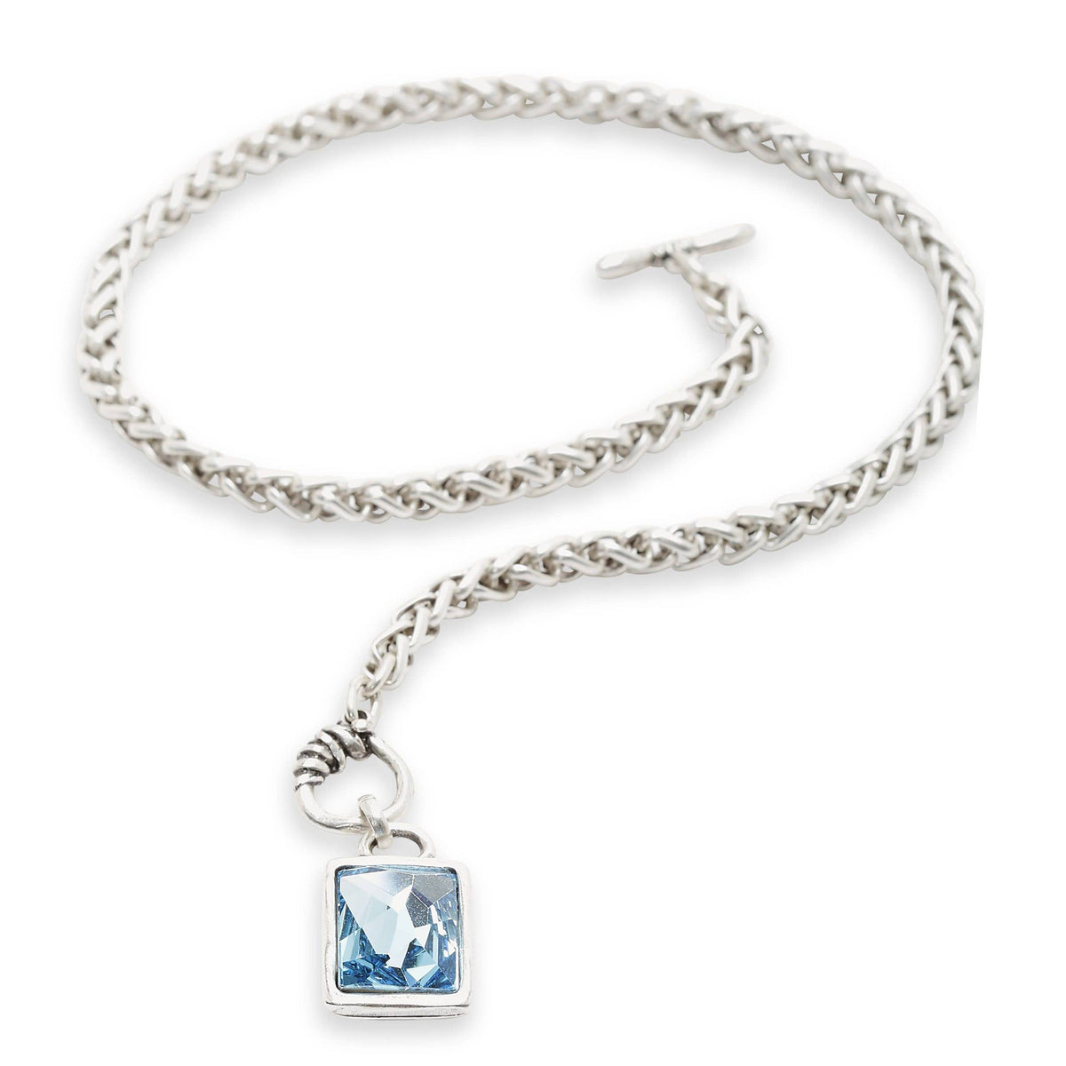 A silver-toned braided chain bracelet with a toggle clasp and a dangling square pendant featuring a light blue faceted gemstone, shown on a plain white background.