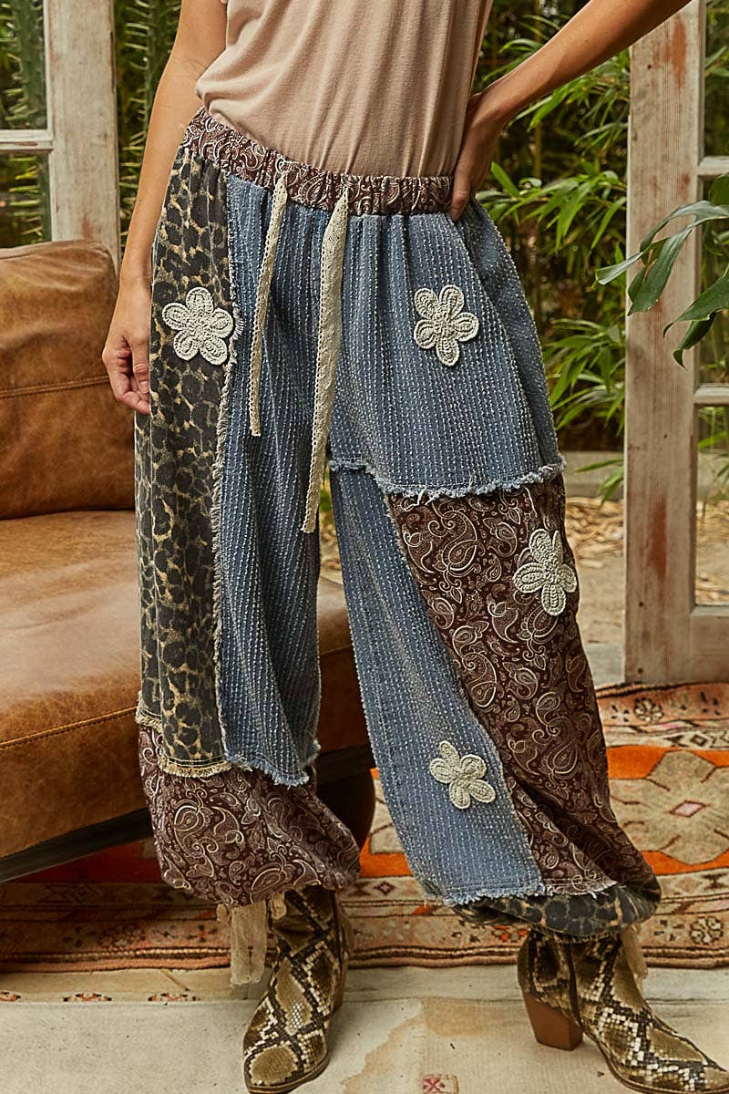 Person wearing patchwork pants with floral and animal print details indoors.