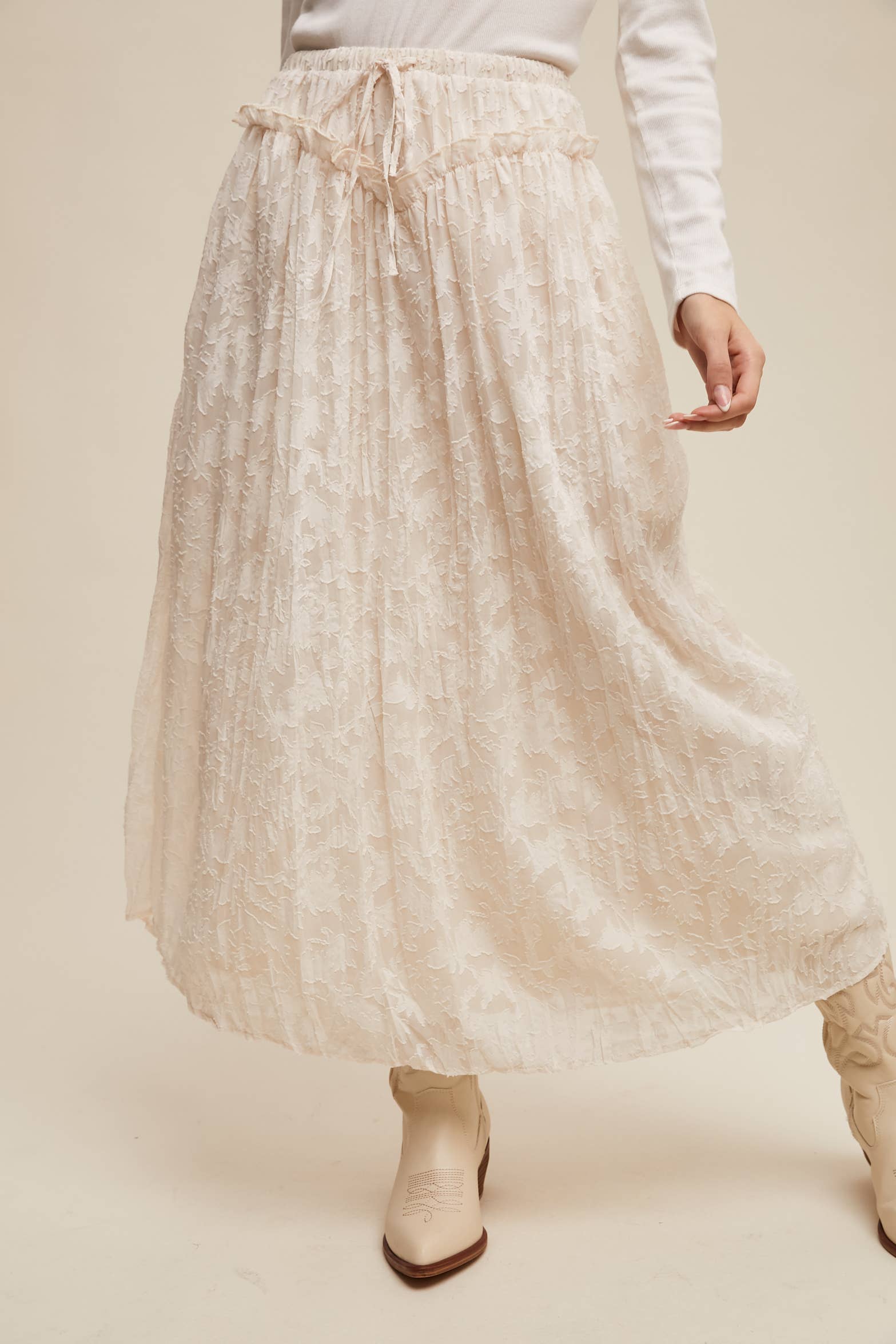 Ivory floral lace maxi skirt with elastic drawstring waist and ruffle detail, ankle-length bubble hem; shown on model with cream western boots.