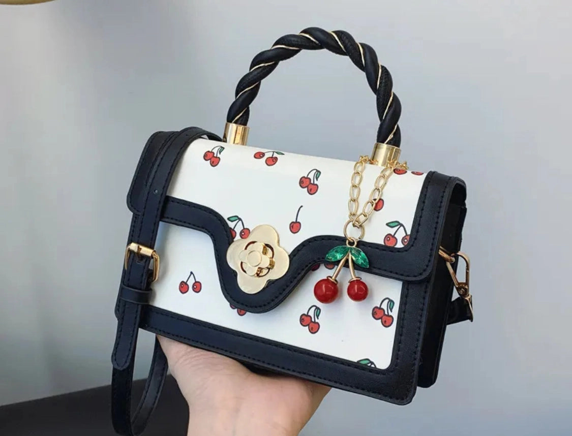 Handbag  in black and white  with a cherry design held by a hand against a neutral background