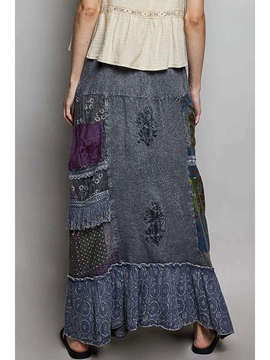 Close-up front detail, slate blue base with purple/olive/navy panels, lace trim + fringe + ruffled hem