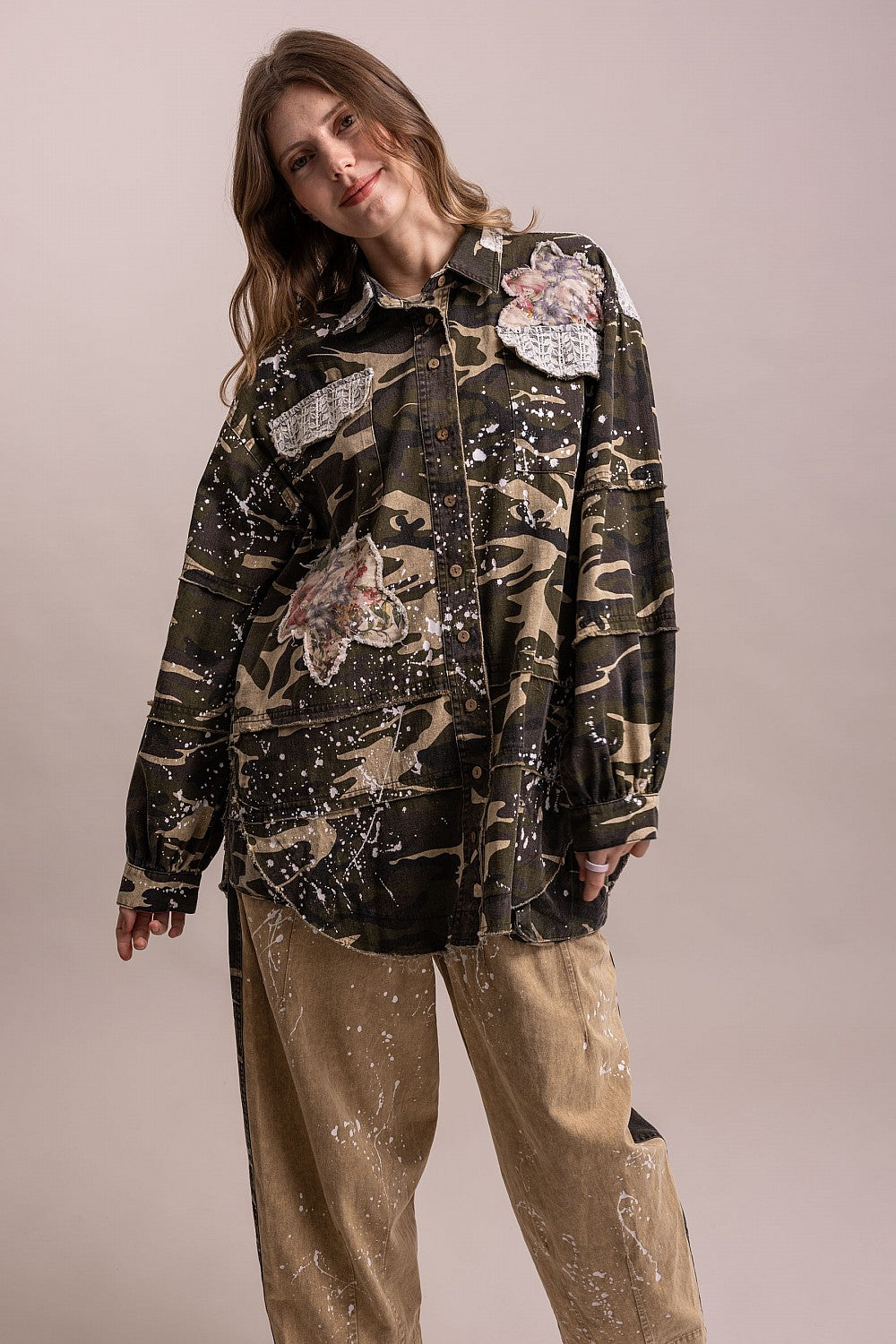 Angled front view of BlueVelevet camo patchwork jacket showing its loose silhouette, floral patches and curved hem.