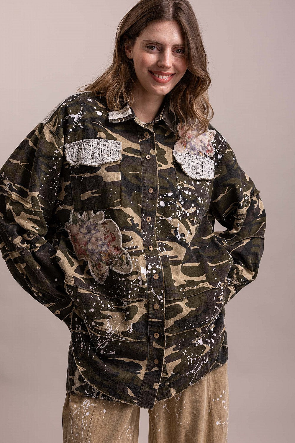 BlueVelevet camo patchwork jacket with hands at hips, showing floral appliques and white splatter detailing.