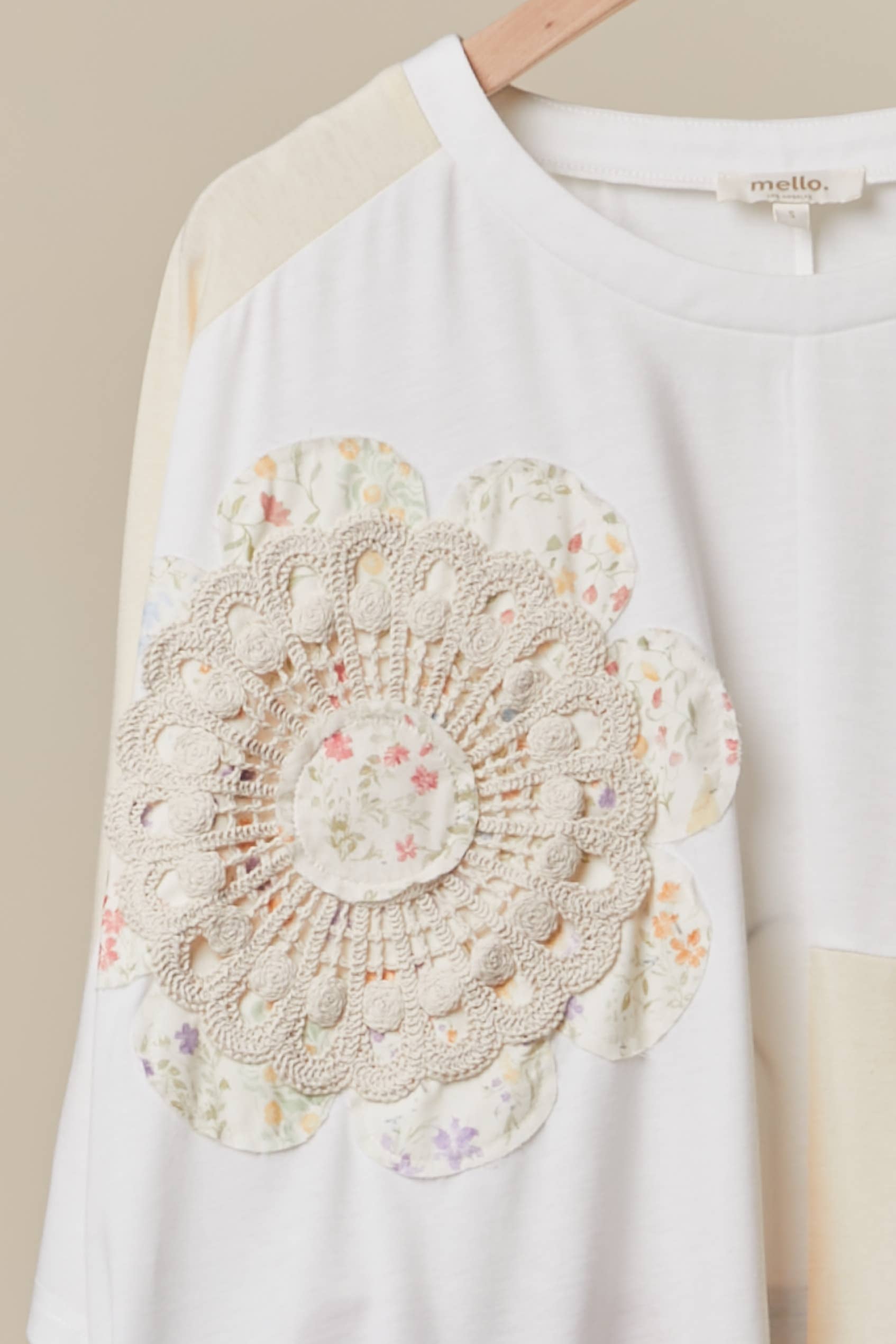 Close up of patchwork crochet The Cleo Crochet Patchwork Top in Cream — oversized patchwork silhouette with crochet medallion patch and flower appliqué detail, boho-luxe ivory and cream colorblock top