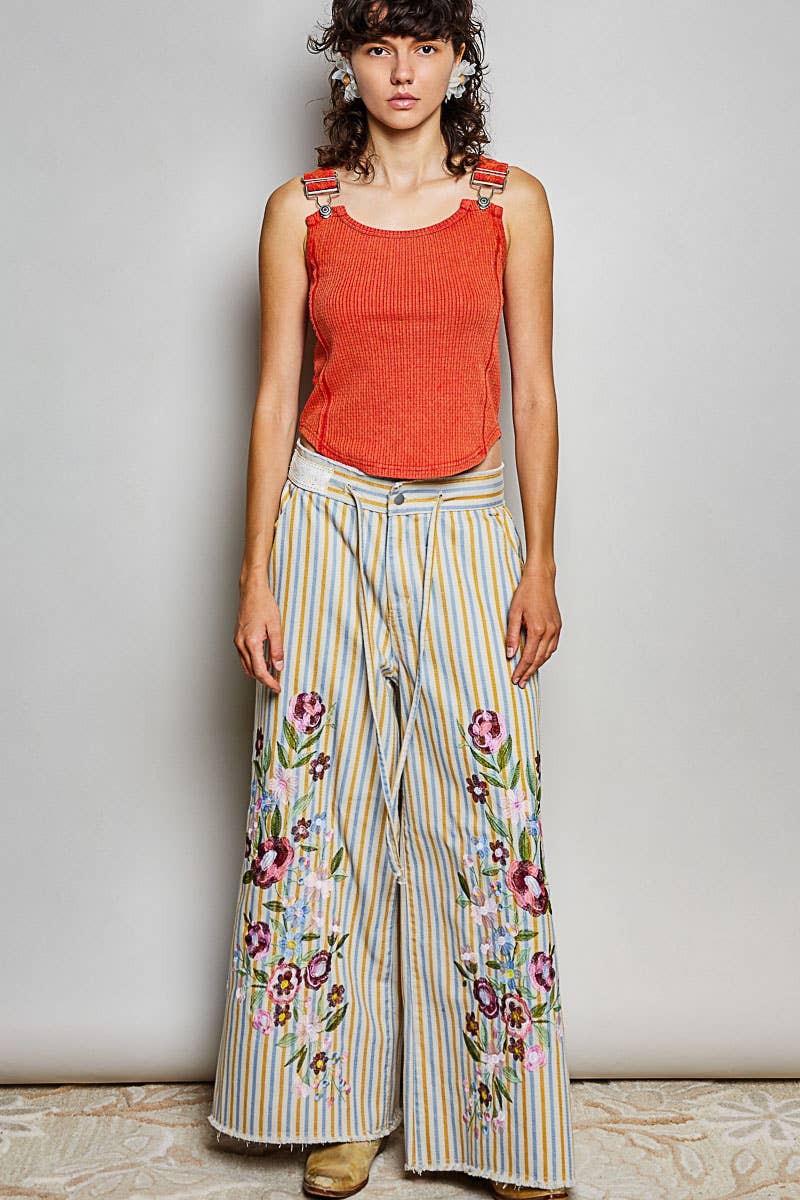 Model wearing Marigold Revival floral embroidered striped wide-leg jeans with a coral tank top and tan shoes.

