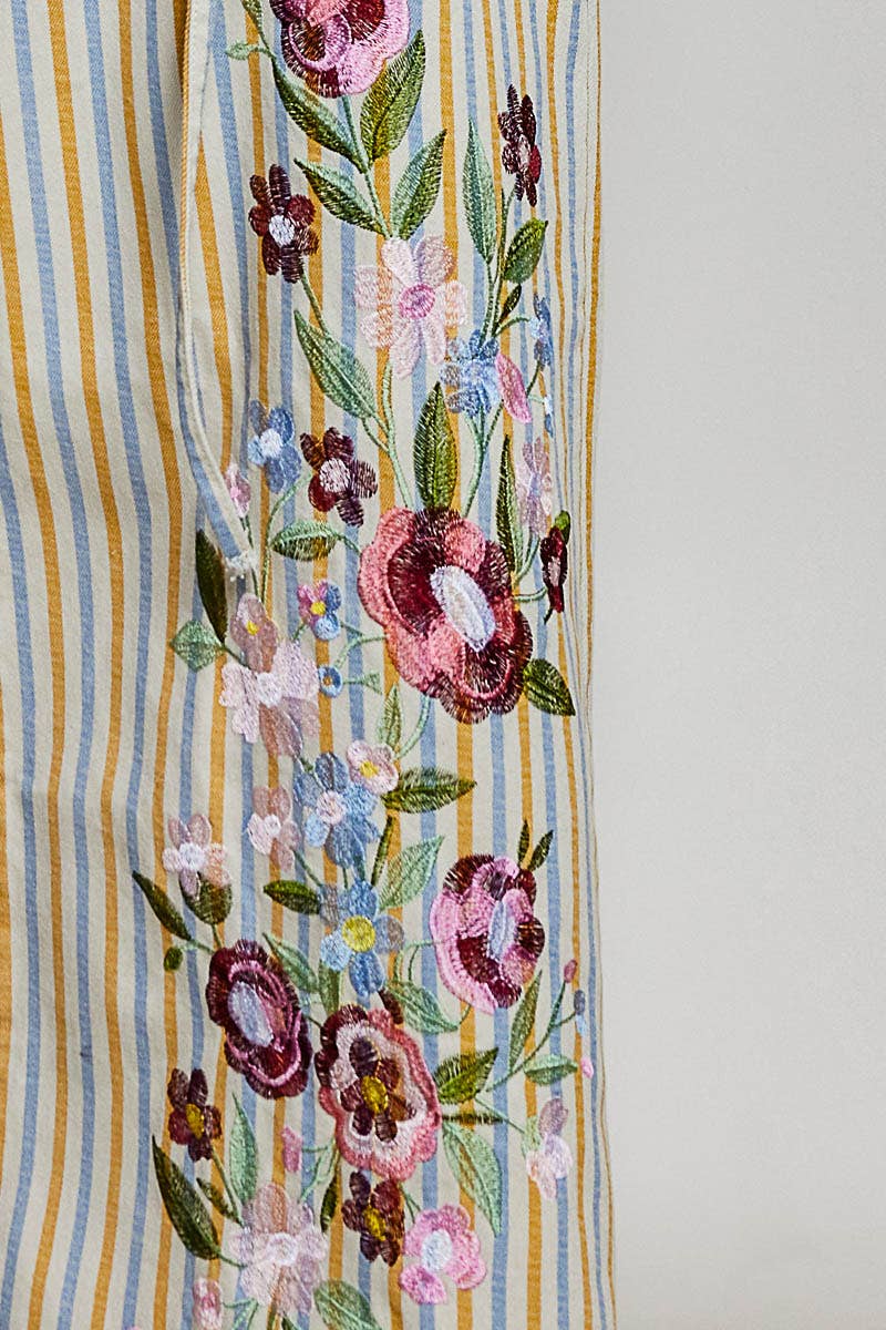 Close-up of pink, burgundy and blue floral embroidery with green leaves on Marigold Revival mustard and blue striped jeans.

