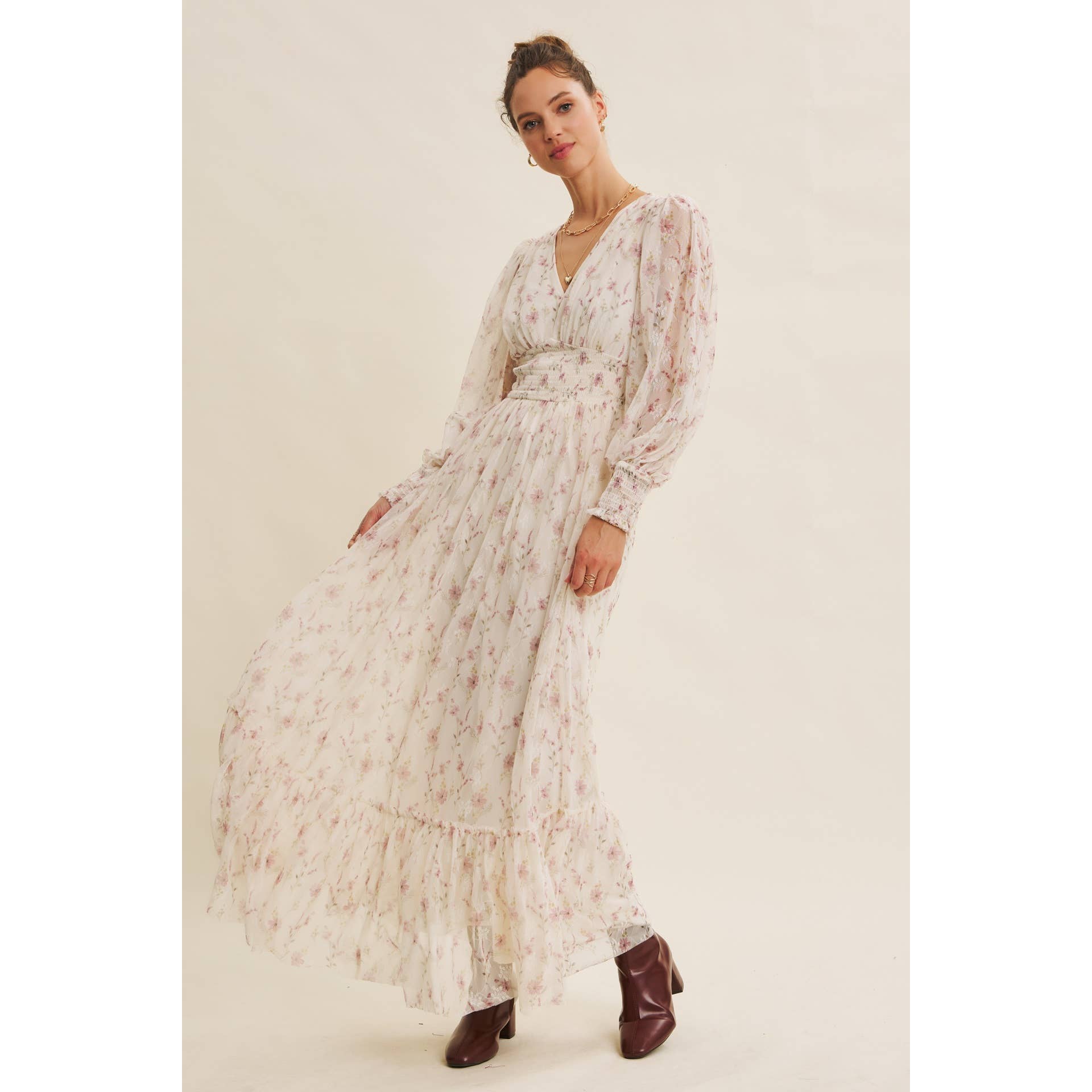 Front view — cream floral chiffon maxi dress with V-neck, sheer long sleeves, smocked waist, and ruffle hem; styled with brown boots.