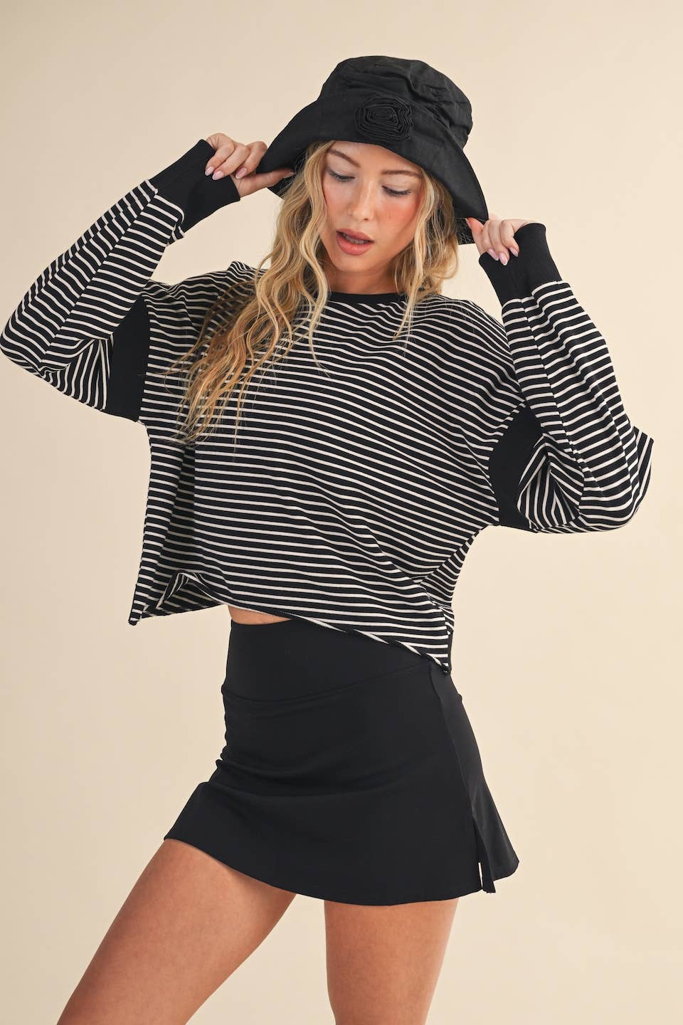 Woman wearing a black and white striped sweater with a black skirt and hat on a beige background
