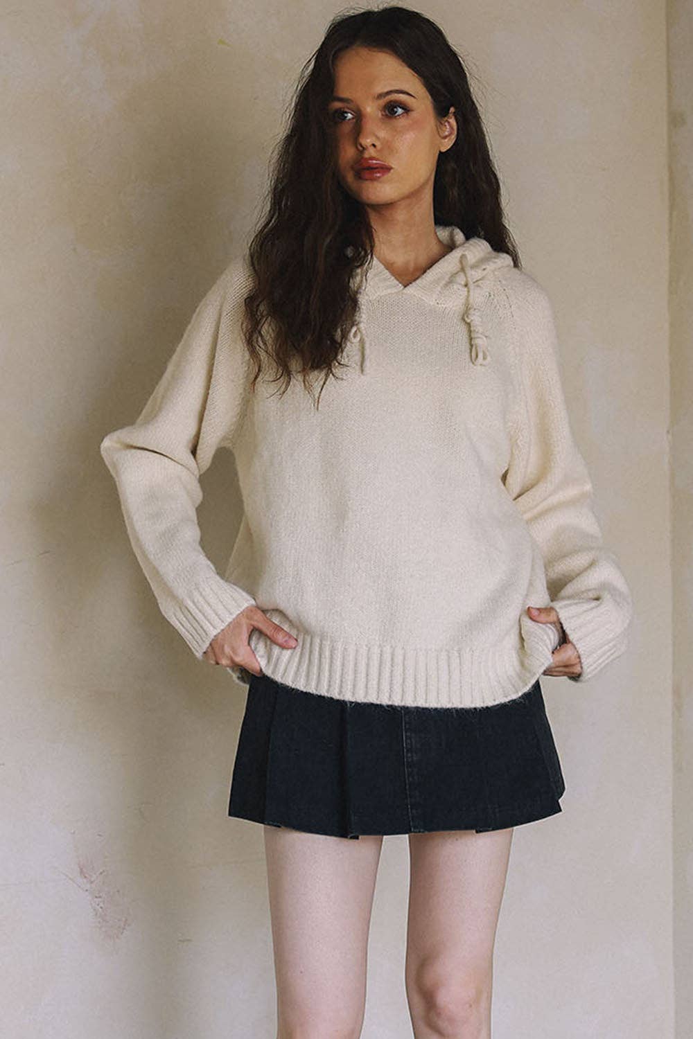 Woman wearing a white hoodie and black skirt against a plain background